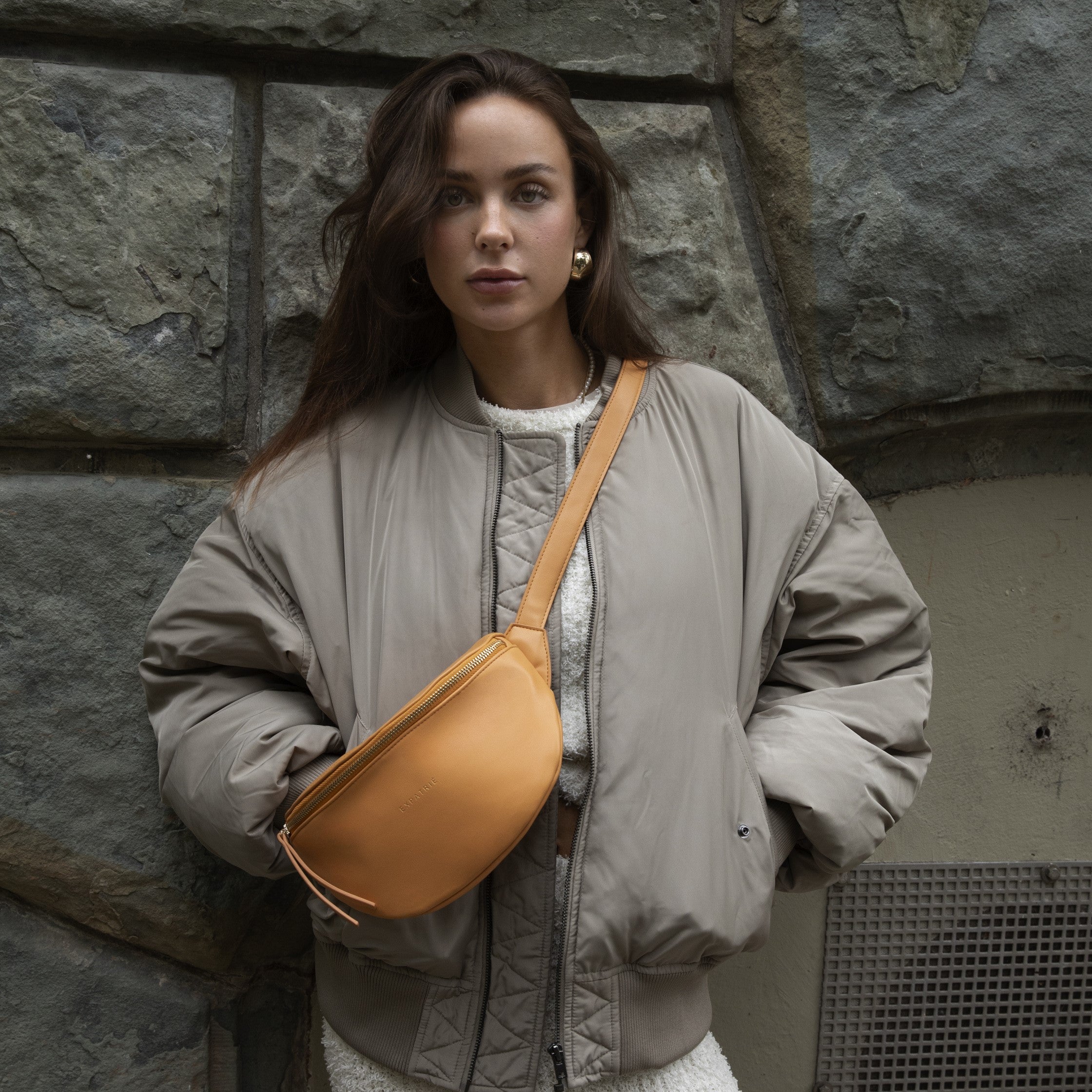 Frau trägt beige Jacke und orangefarbene Bauchtasche 'Alice Small' von Expatrié
