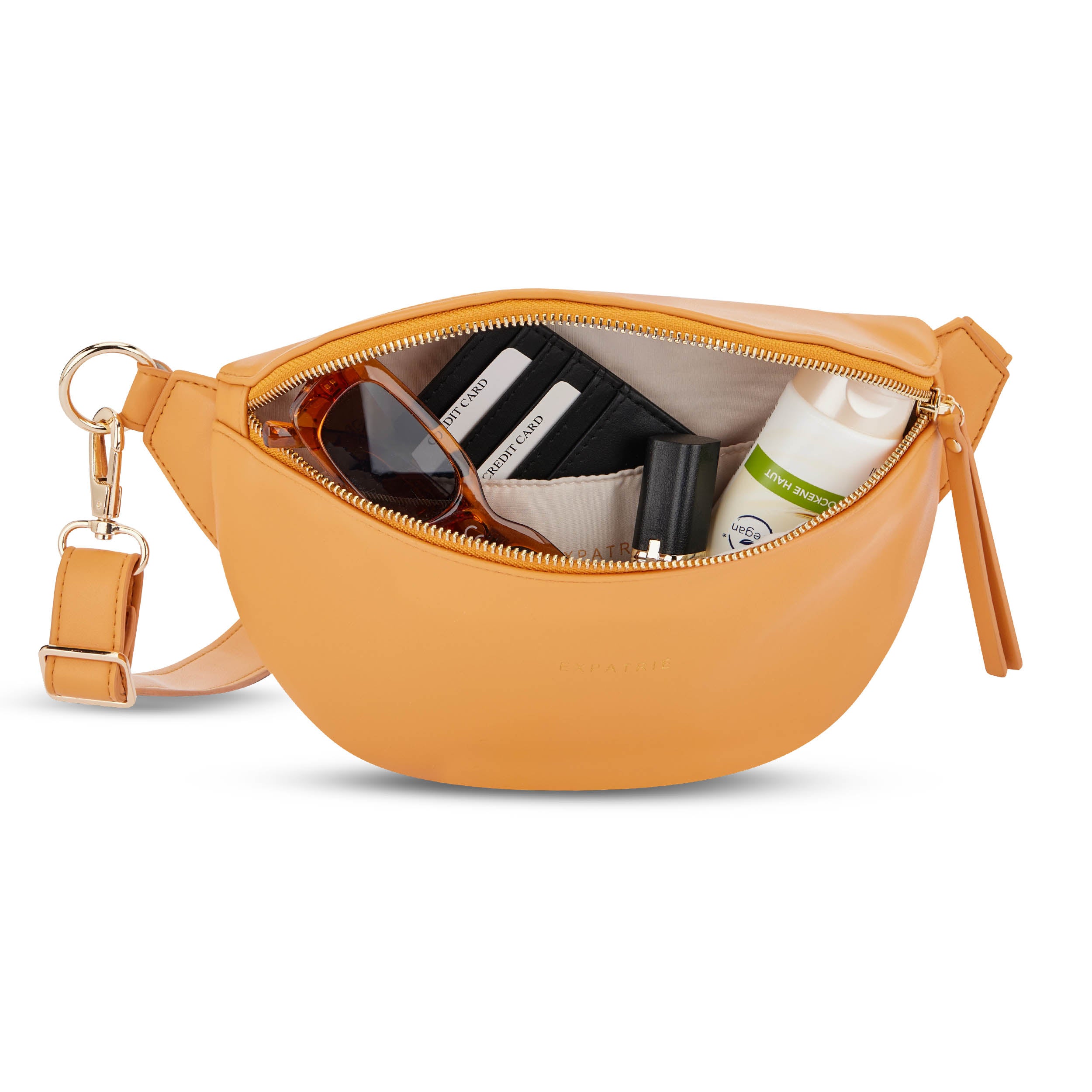 Orangefarbene Bauchtasche 'Alice Small' mit geöffnetem Reißverschluss, darin Sonnenbrille, Kreditkartenetui, Lippenstift und Handcreme