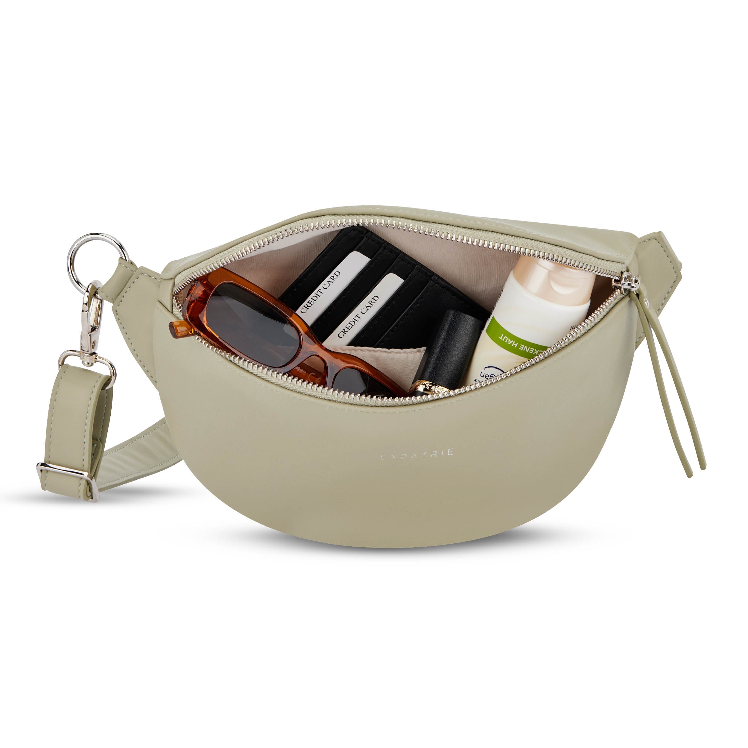 Palegrüne Bauchtasche Alice Small mit geöffneter Reißverschlusstasche, enthält Sonnenbrille, Lippenstift, Tube Creme und Kartenetui