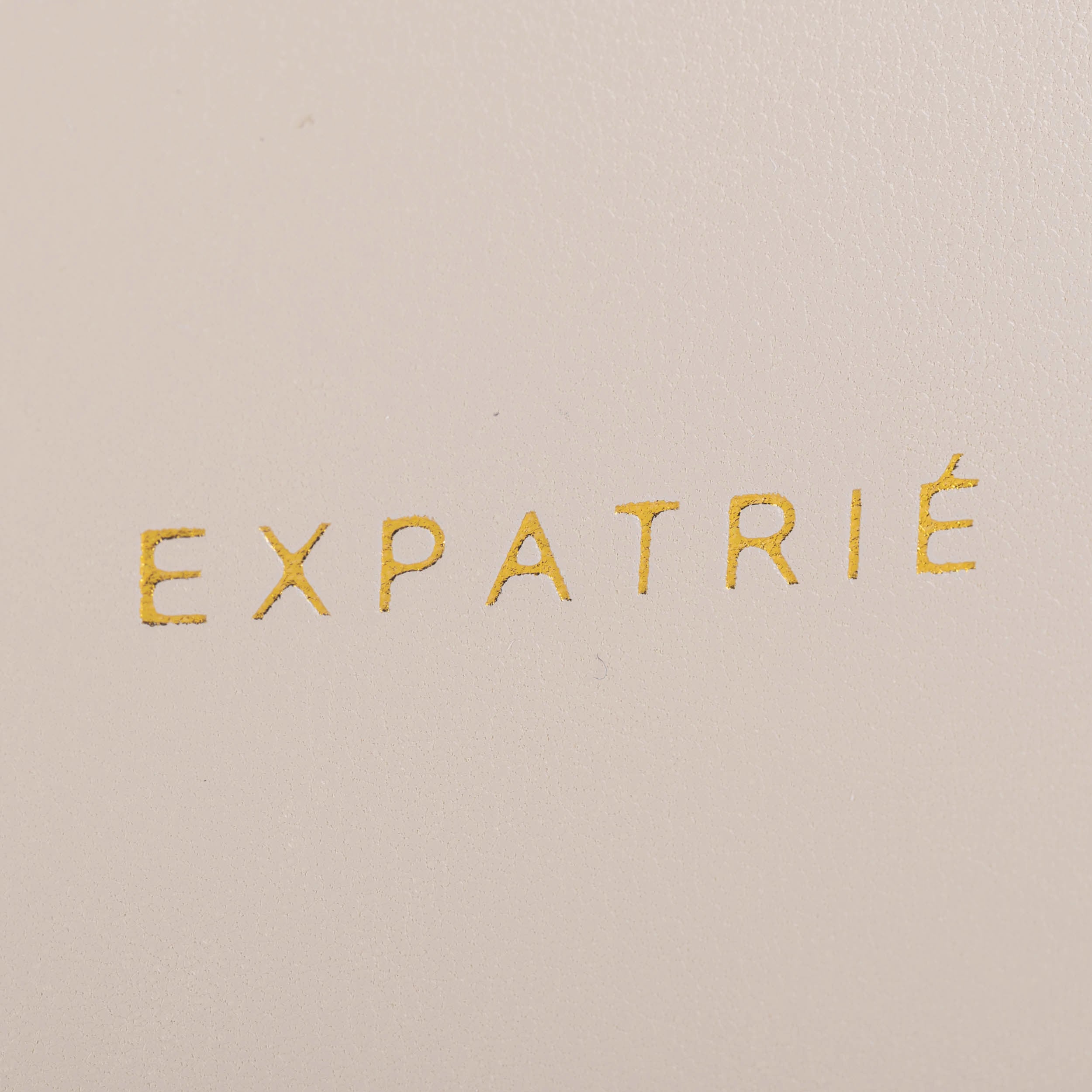 Goldene Prägung mit dem Schriftzug 'EXPATRIÉ' auf beigefarbenem Leder