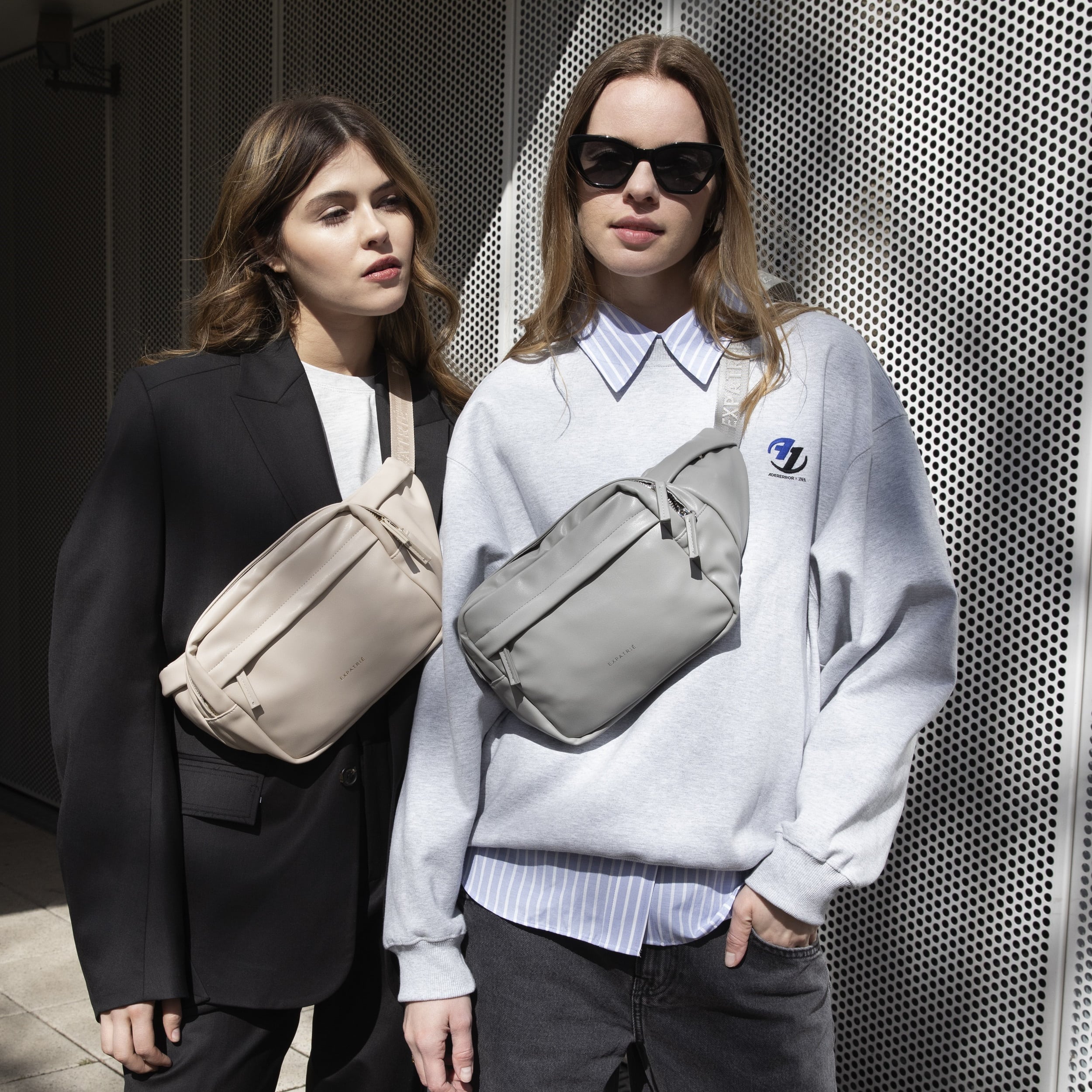 Zwei Frauen mit grauer und beiger Bauchtasche Justine PU aus Kunstleder vor Metallwand