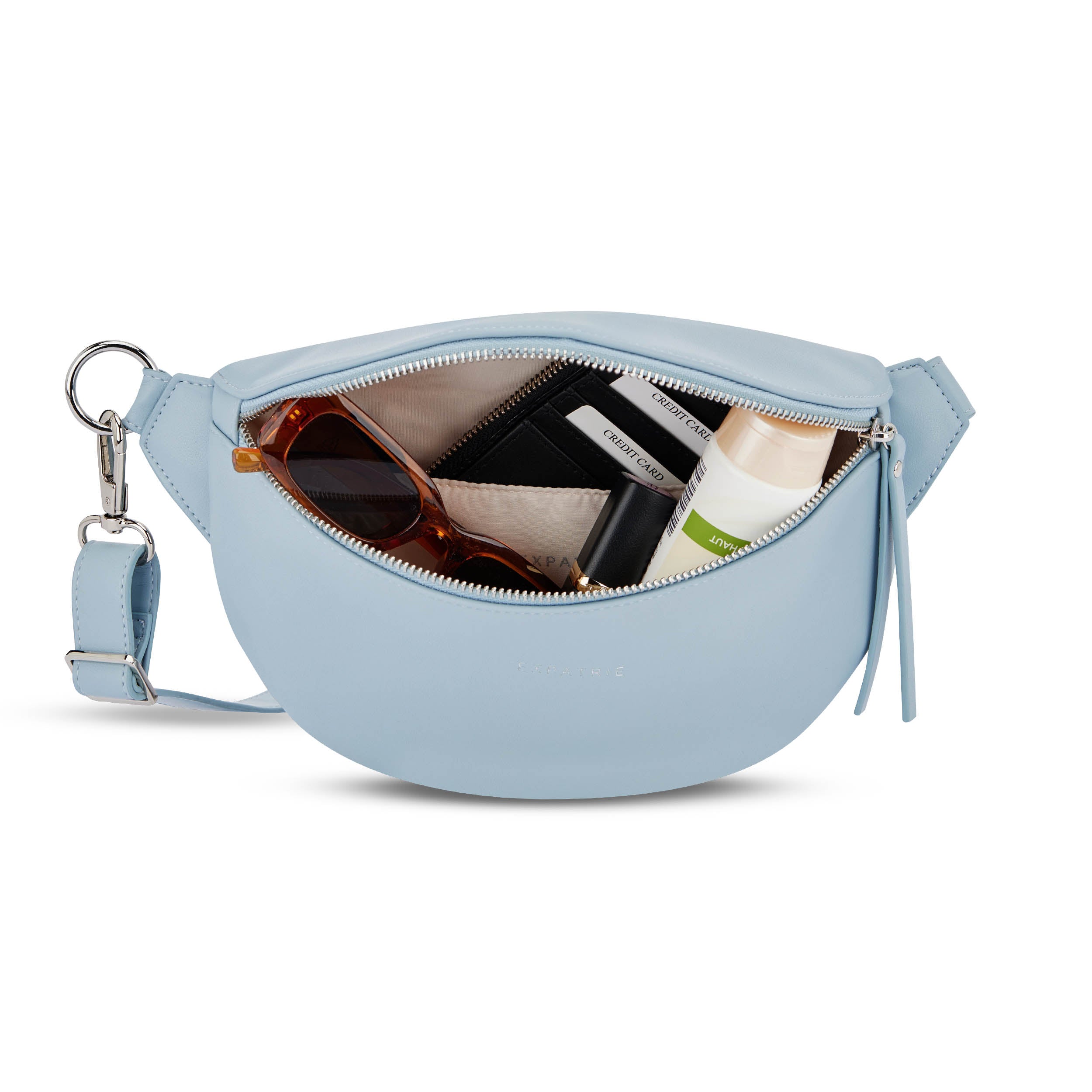 Hellblaue Bauchtasche Alice Small mit Reißverschluss, geöffnet mit Sonnenbrille, Kreditkartenetui und Kosmetikflasche innen