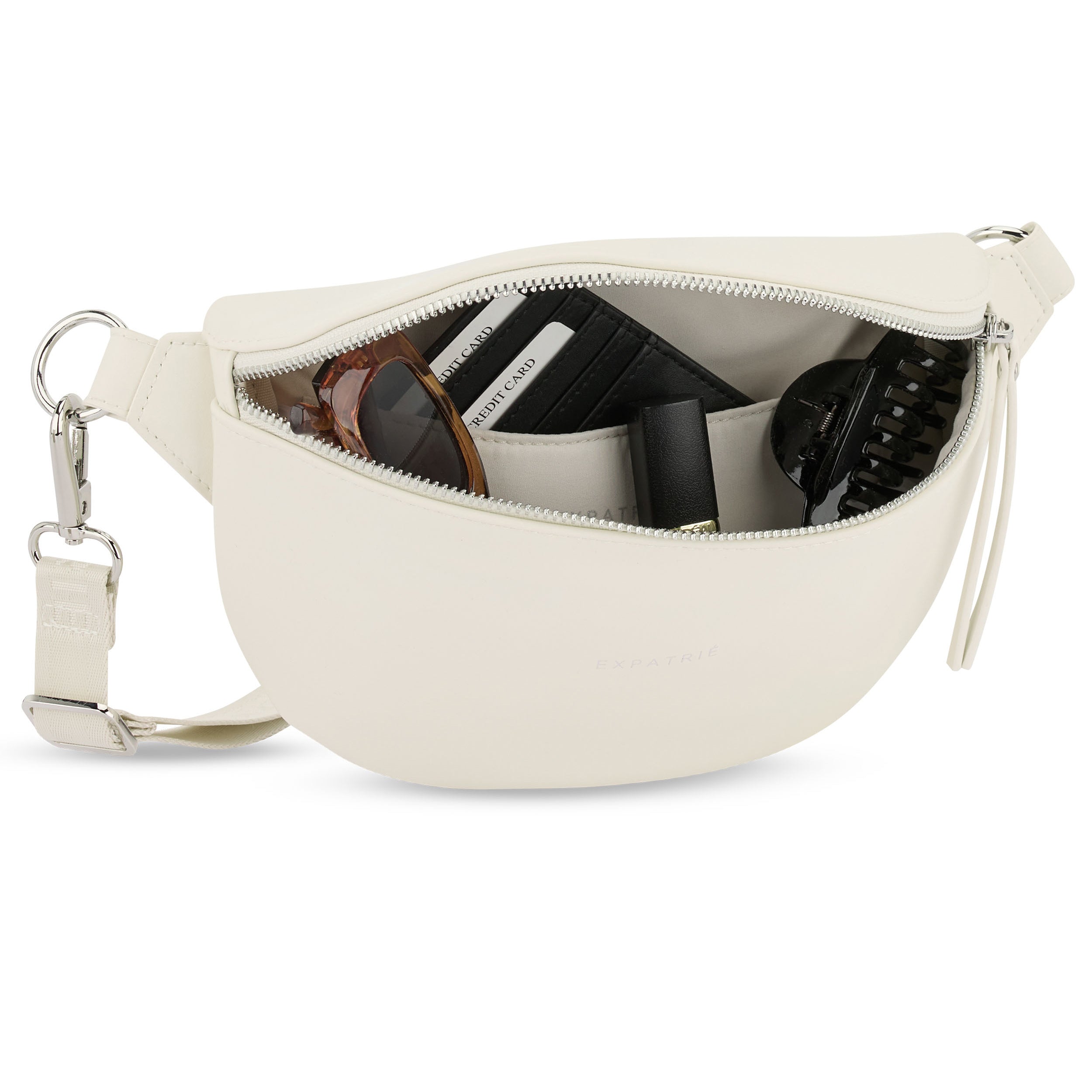 Weiße Bauchtasche 'Alice Small' mit geöffnetem Reißverschluss, gefüllt mit Sonnenbrille, Kreditkarten, Lippenstift und Haarklammer