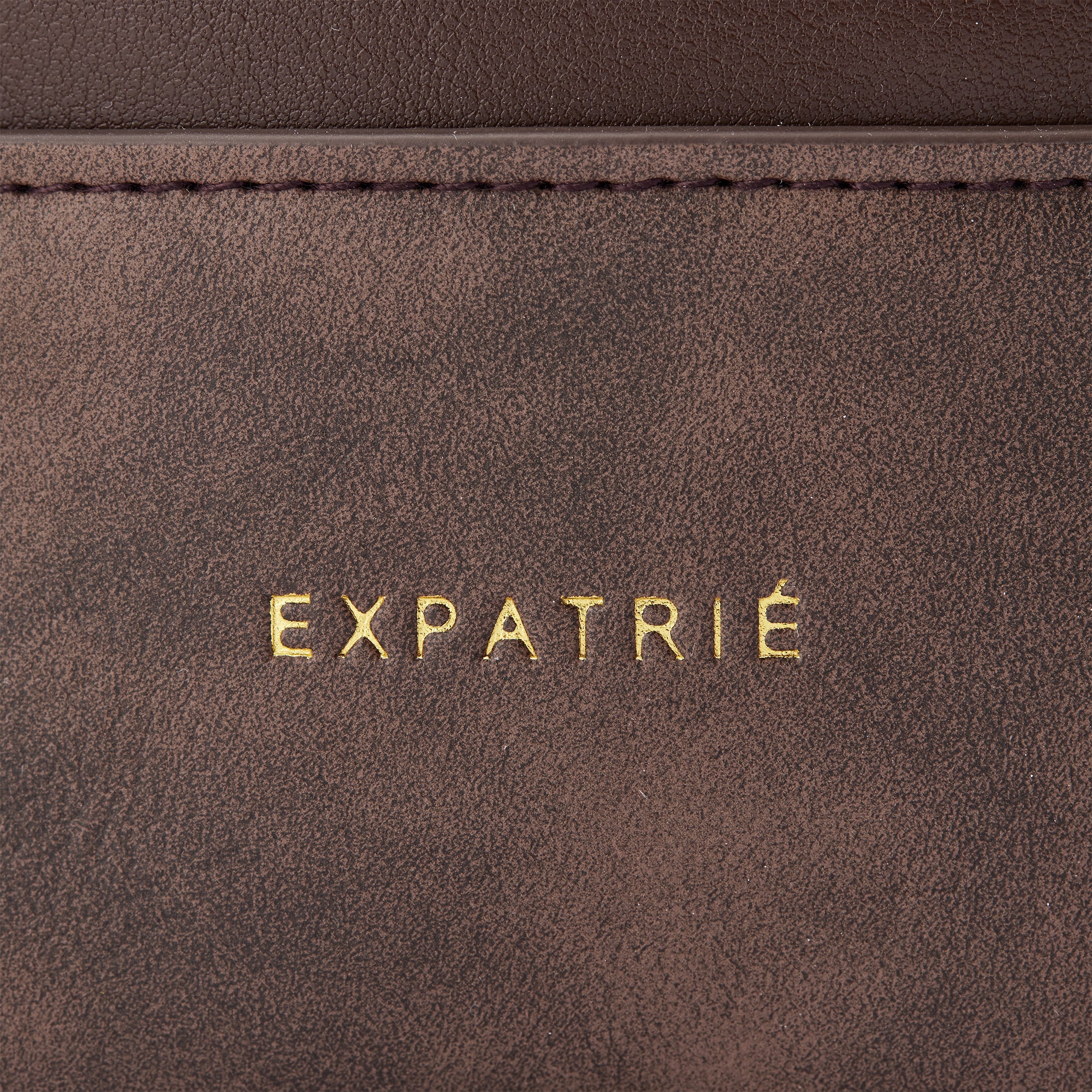 Feine goldene Prägung 'EXPATRIÉ' auf braunem Leder der Beuteltasche Sarah Small