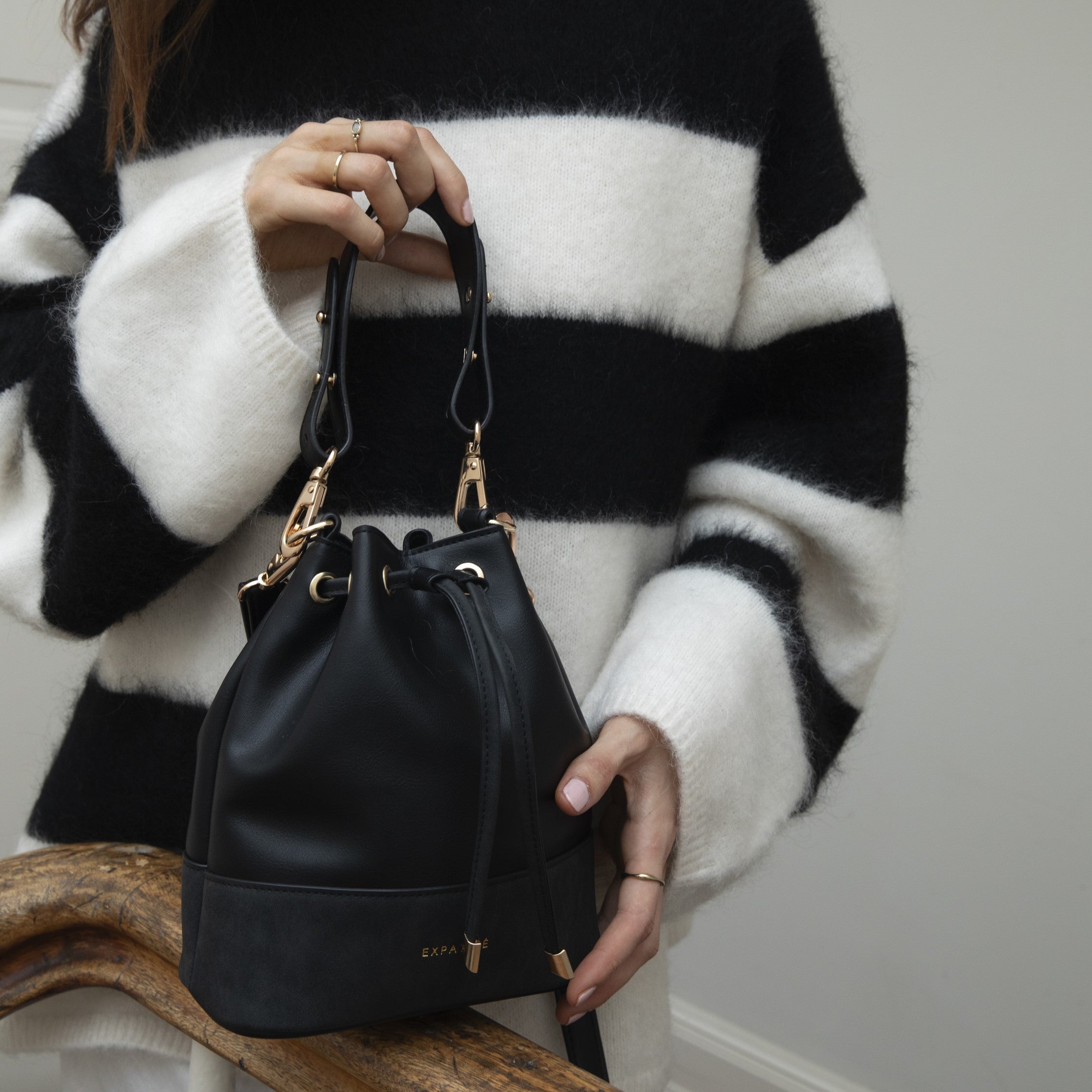 Schwarze Beuteltasche Sarah Small aus Leder, gehalten von Frau in schwarz-weiß gestreiftem Pullover