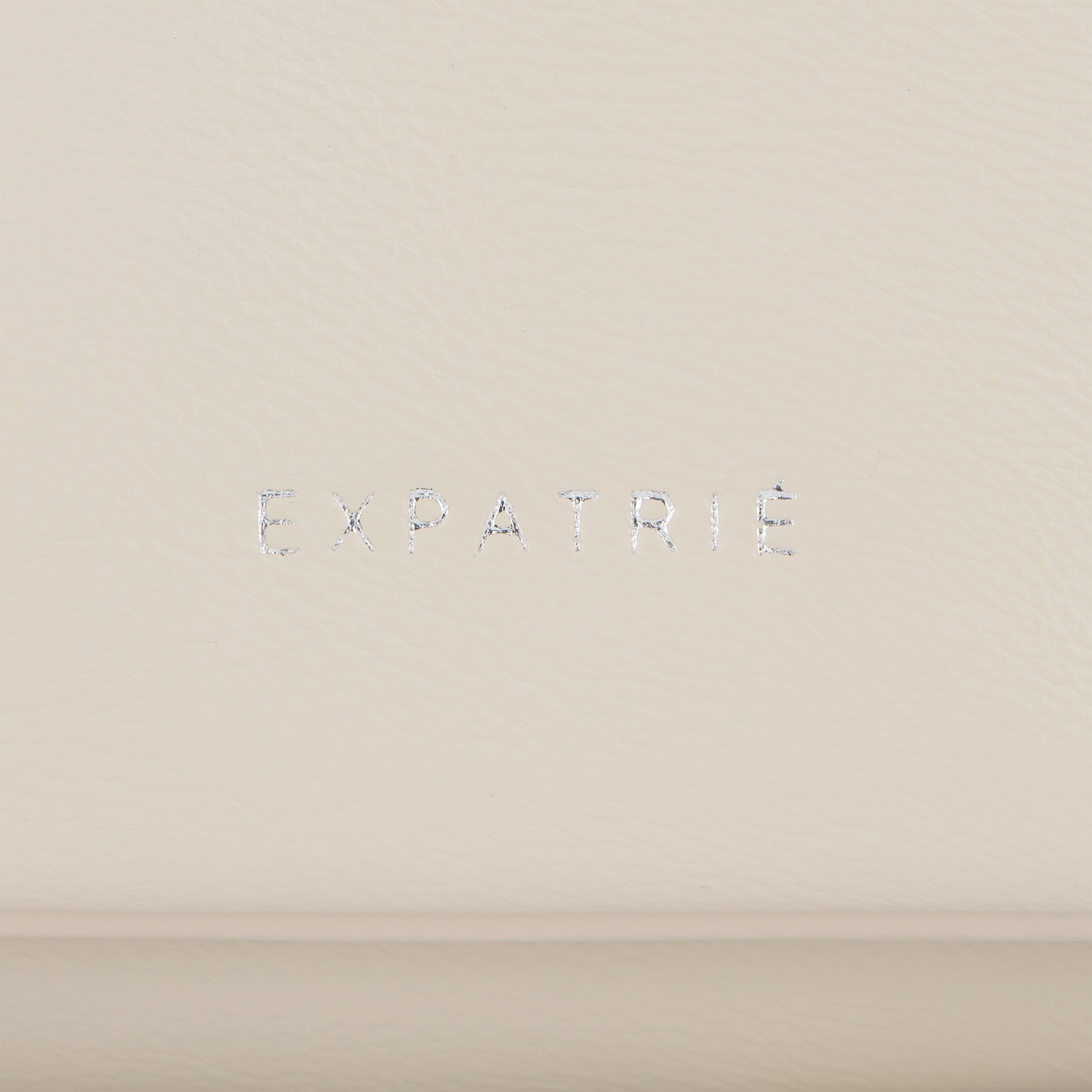 Markenschriftzug 'EXPATRIÉ' auf cremeweißem Kunstleder der Clutch Juliette