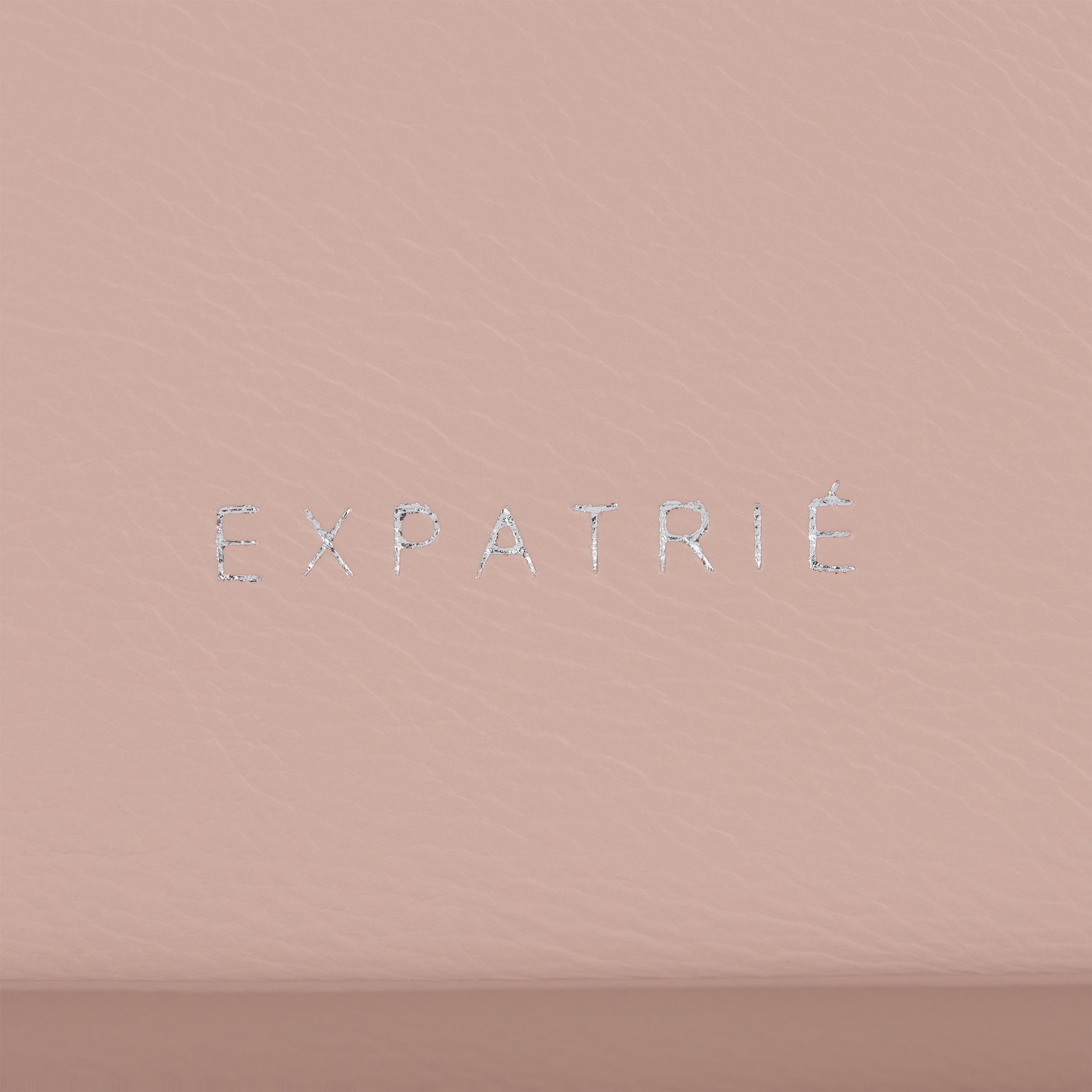 Markenname 'Expatrié' aus silbernen Buchstaben auf rosa Kunstleder