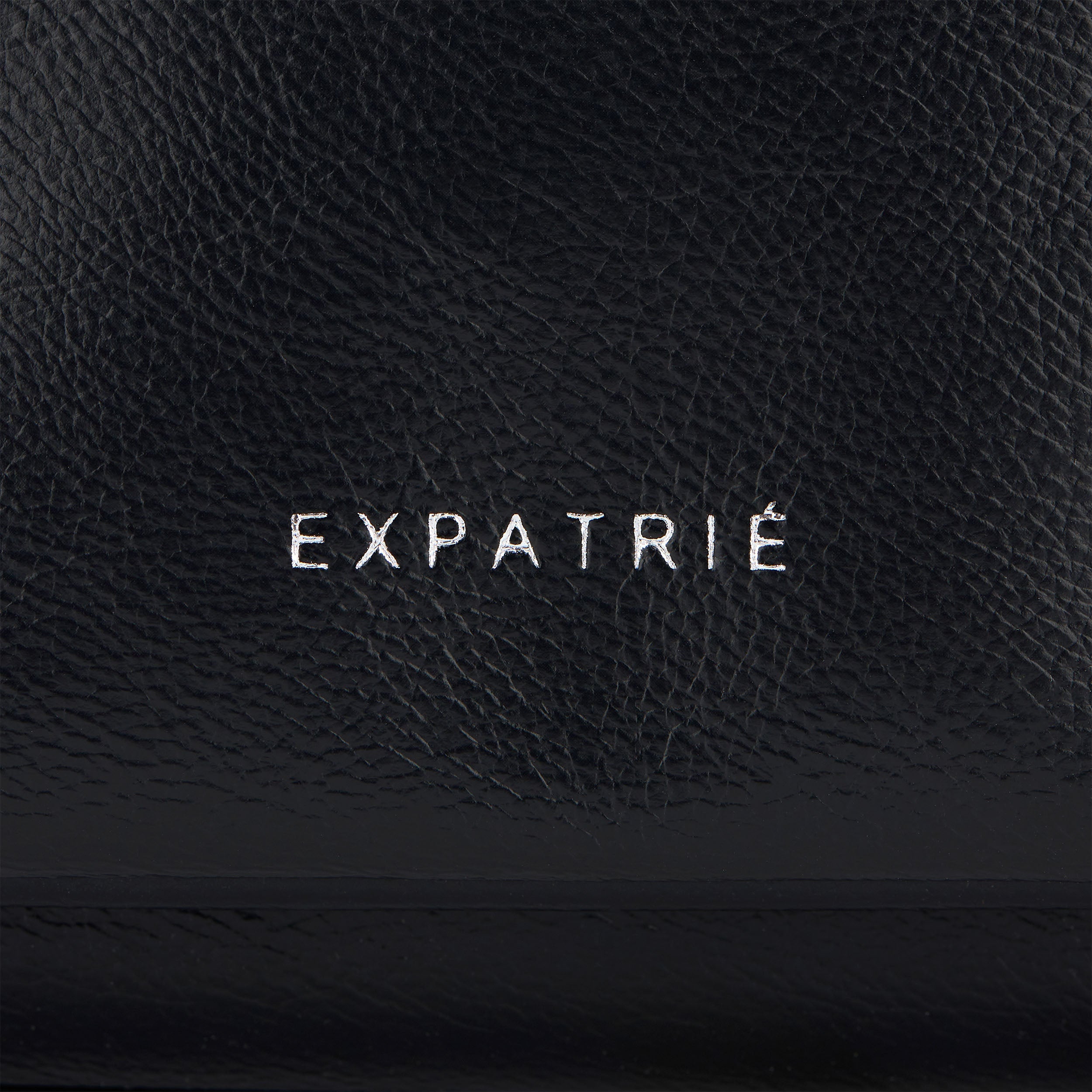 Nahe Ansicht der schwarzen Kunstleder-Clutch Juliette mit weißem 'EXPATRIÉ'-Schriftzug