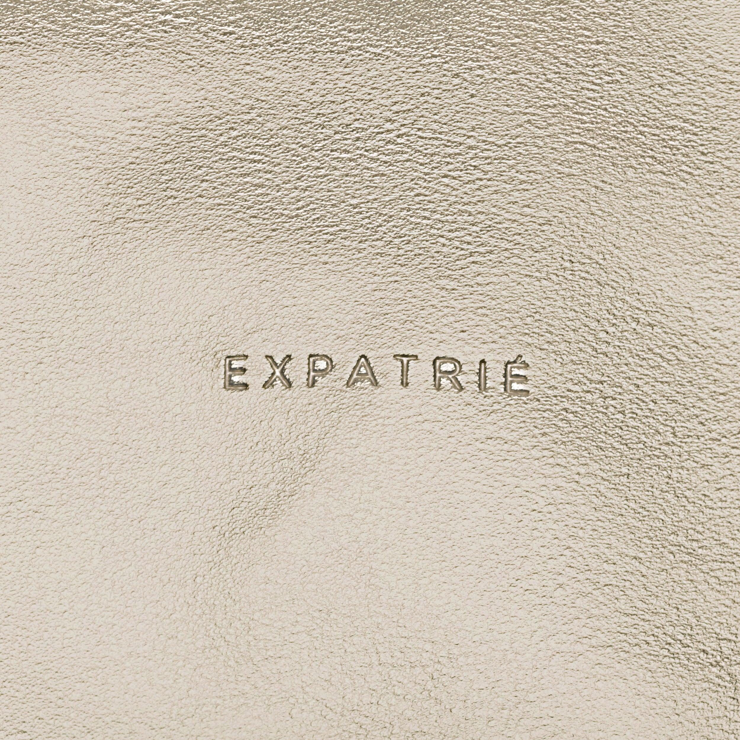 Gold-beige Kunstlederoberfläche der Clutch Emilie mit geprägtem Schriftzug 'Expatrié'