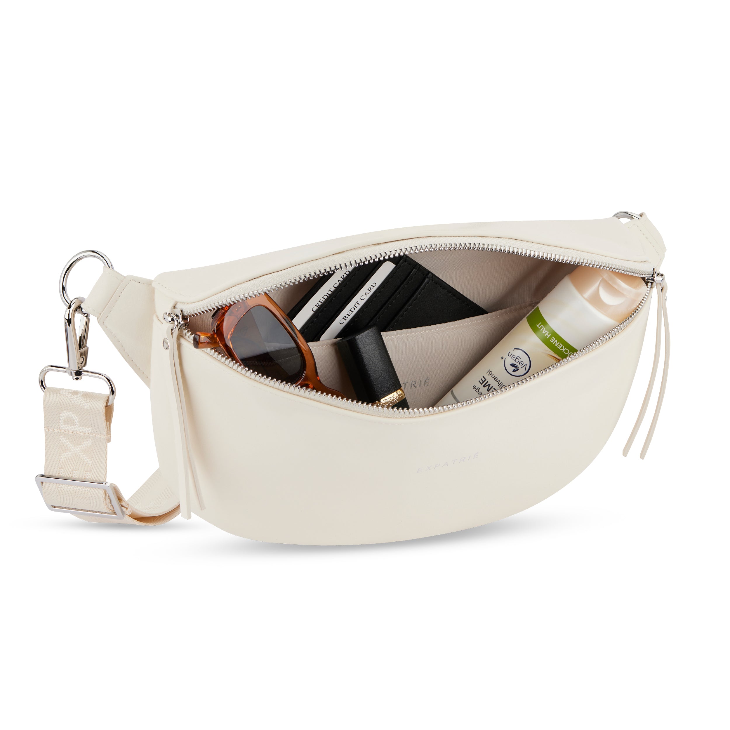 Bauchtasche Alice Medium aus beigem Leder mit Reißverschluss und Innenfächern, gefüllt mit Sonnenbrille, Kreditkartenetui, Lippenstift und Creme
