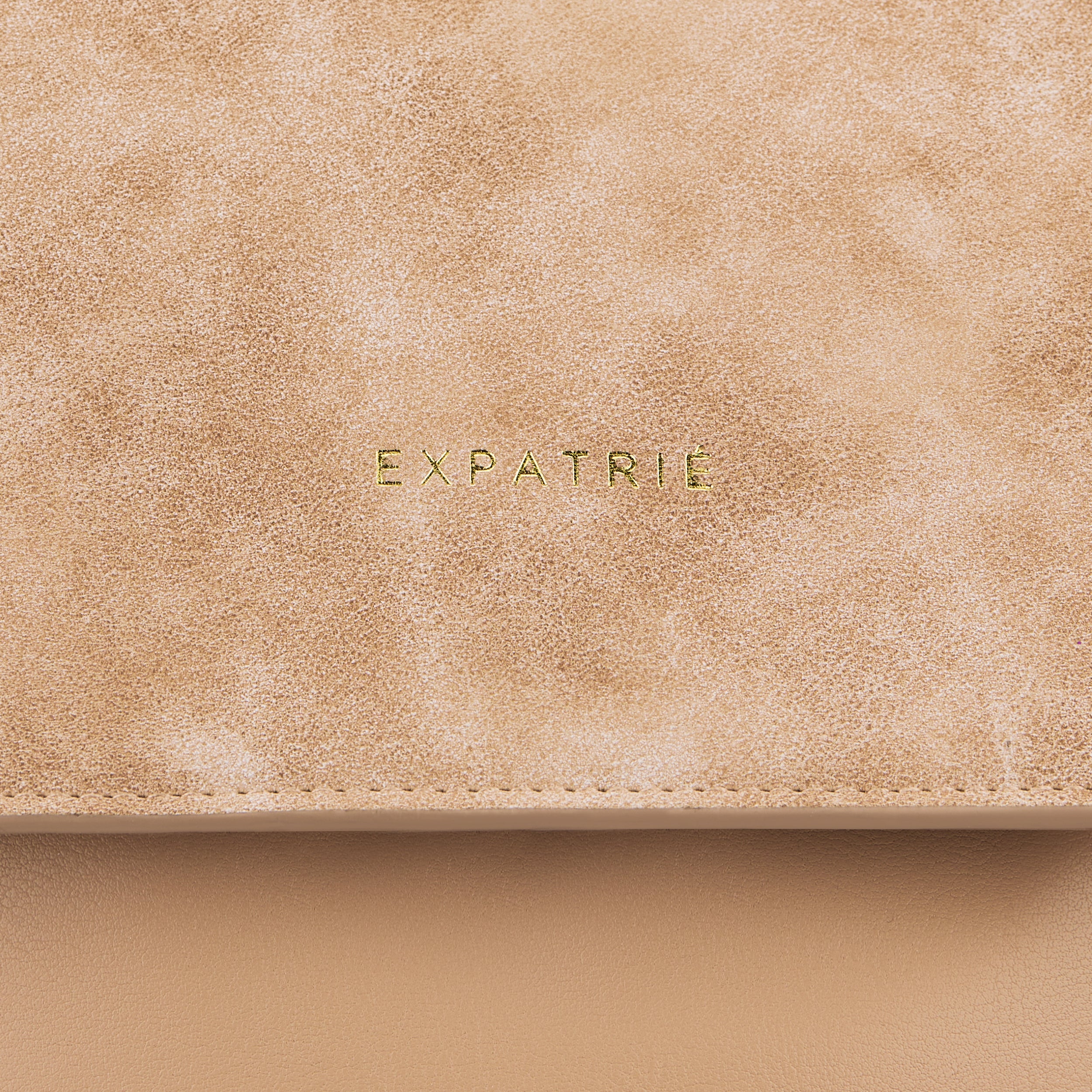 Beige Kunstleder-Oberfläche mit goldfarbenem 'EXPATRIÉ' Schriftzug