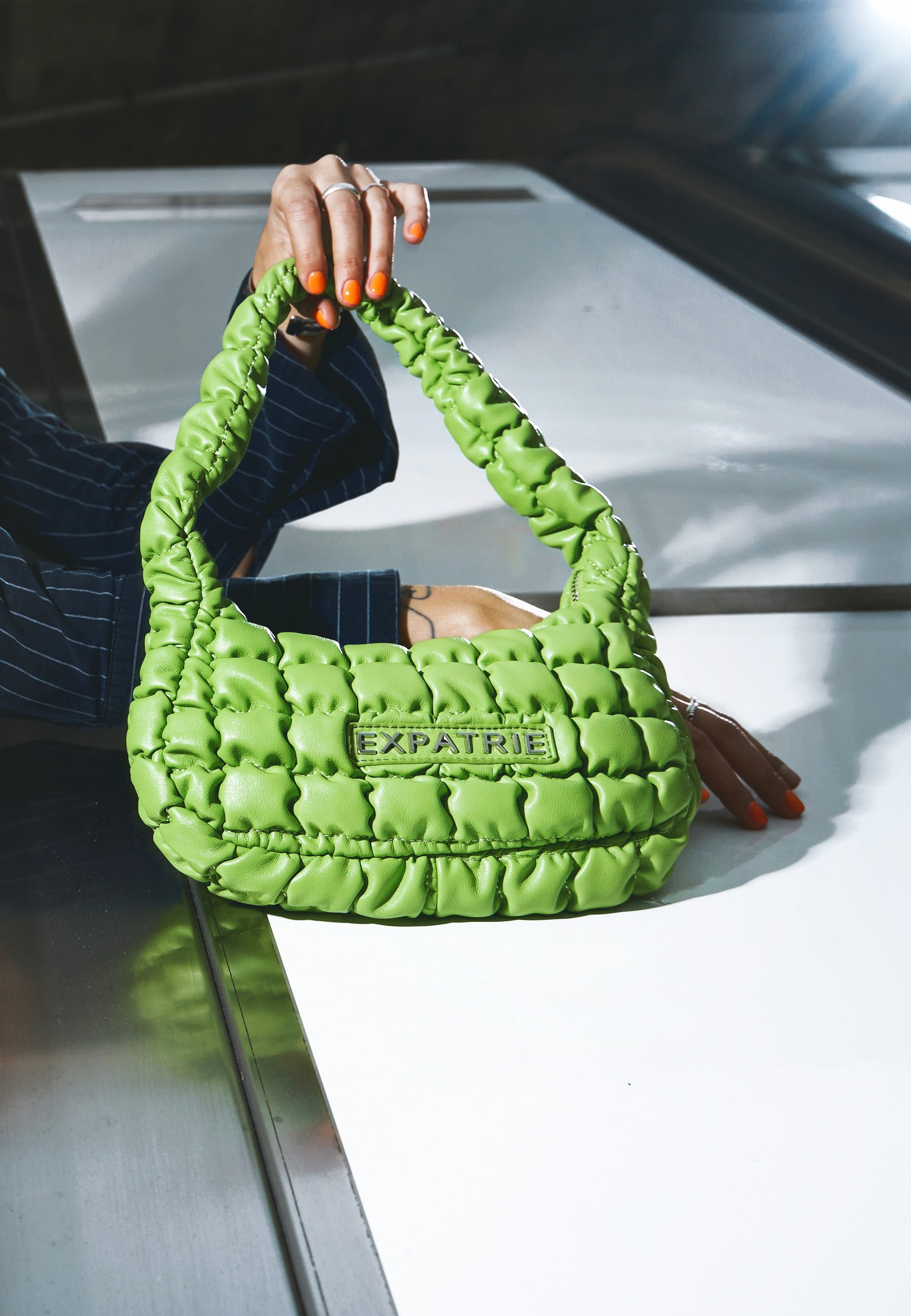 Grüne gesteppte PIPPA SMALL Handtasche von Expatrié mit kurzem Griff, gehalten von Hand mit orangen lackierten Nägeln