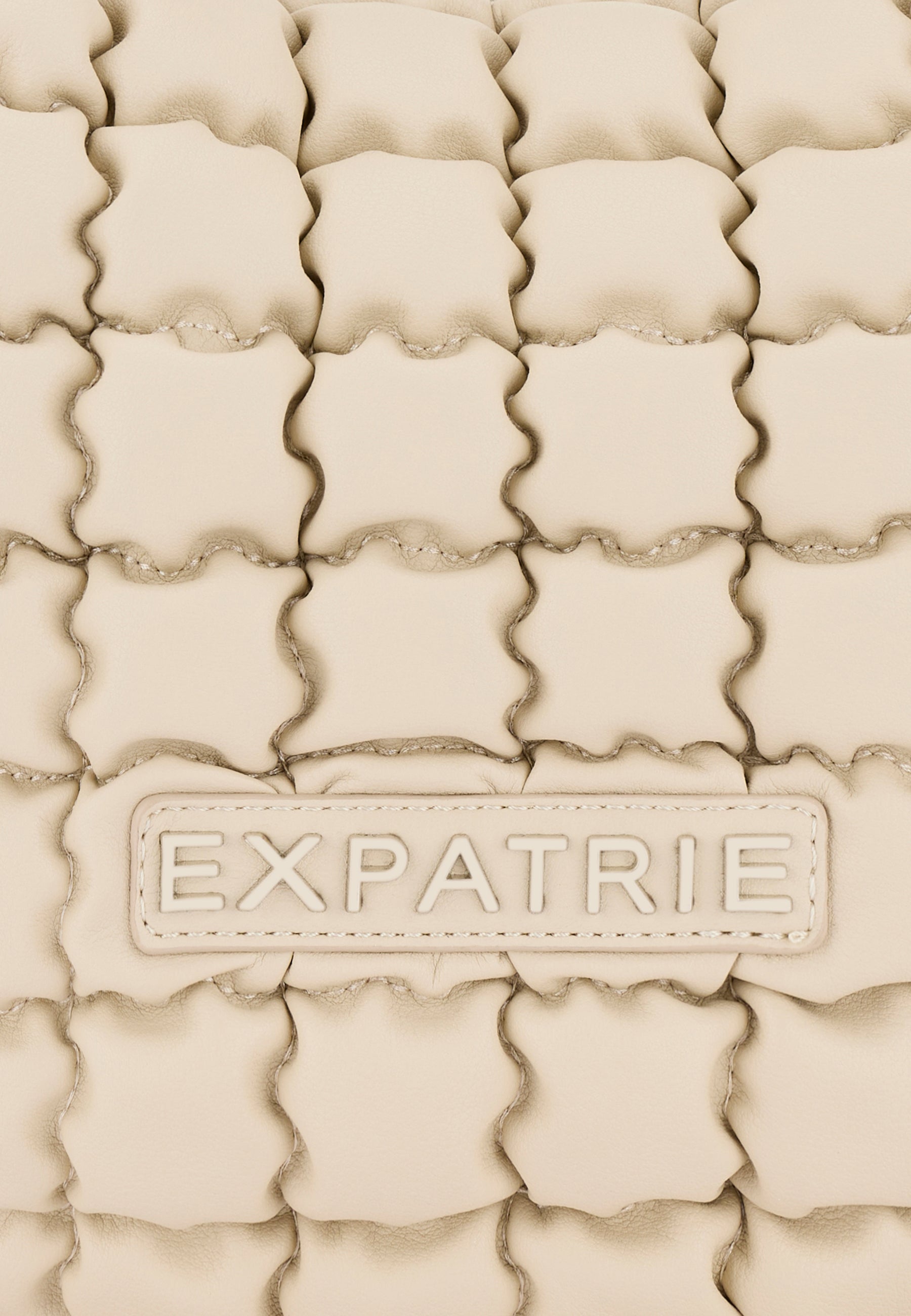 Beige gesteppte Oberfläche mit dem Logo 'EXPATRIE' auf einer PIPPA LARGE Handtasche