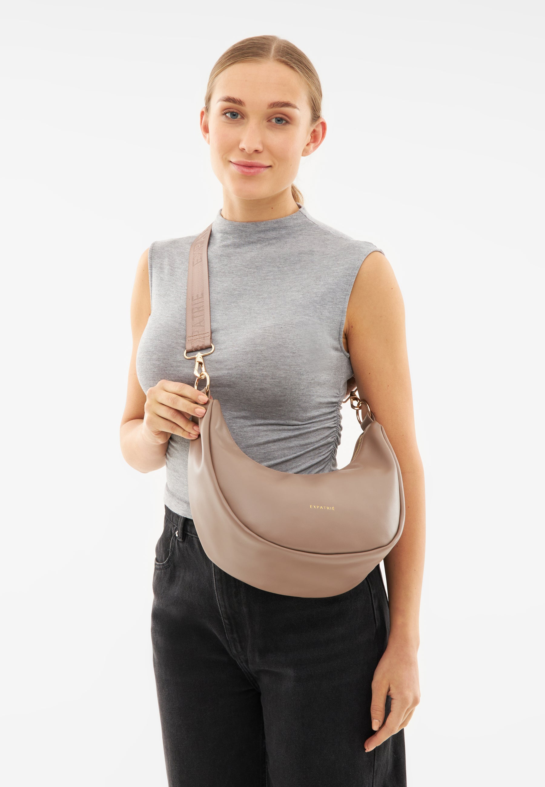 Frau trägt beige-braune LEA MEDIUM Halbmond-Tasche mit verstellbarem Schulterriemen und goldfarbenem Logo