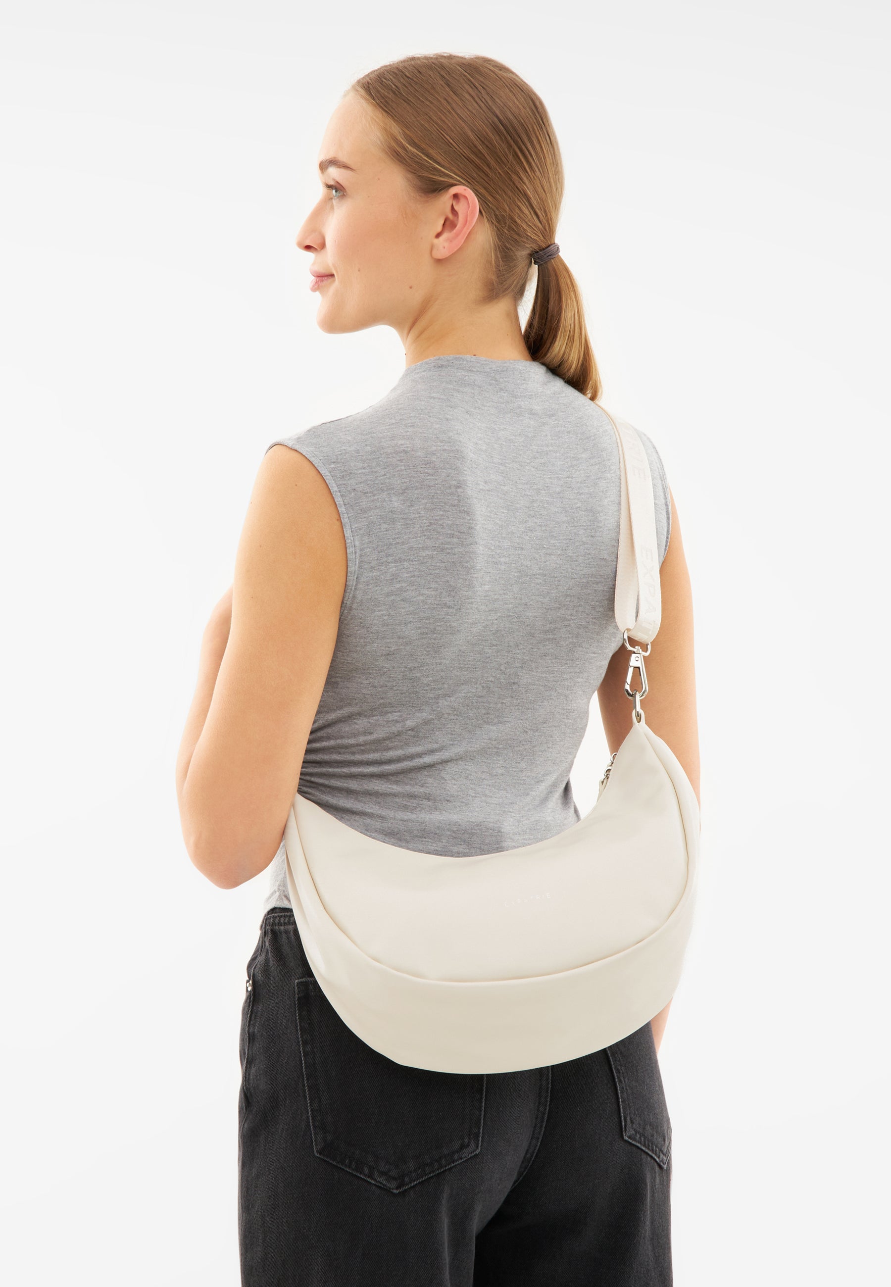 Frau trägt LEA MEDIUM Half Moon Bag in Creme über der Schulter, graues ärmelloses Oberteil, schwarze Jeans