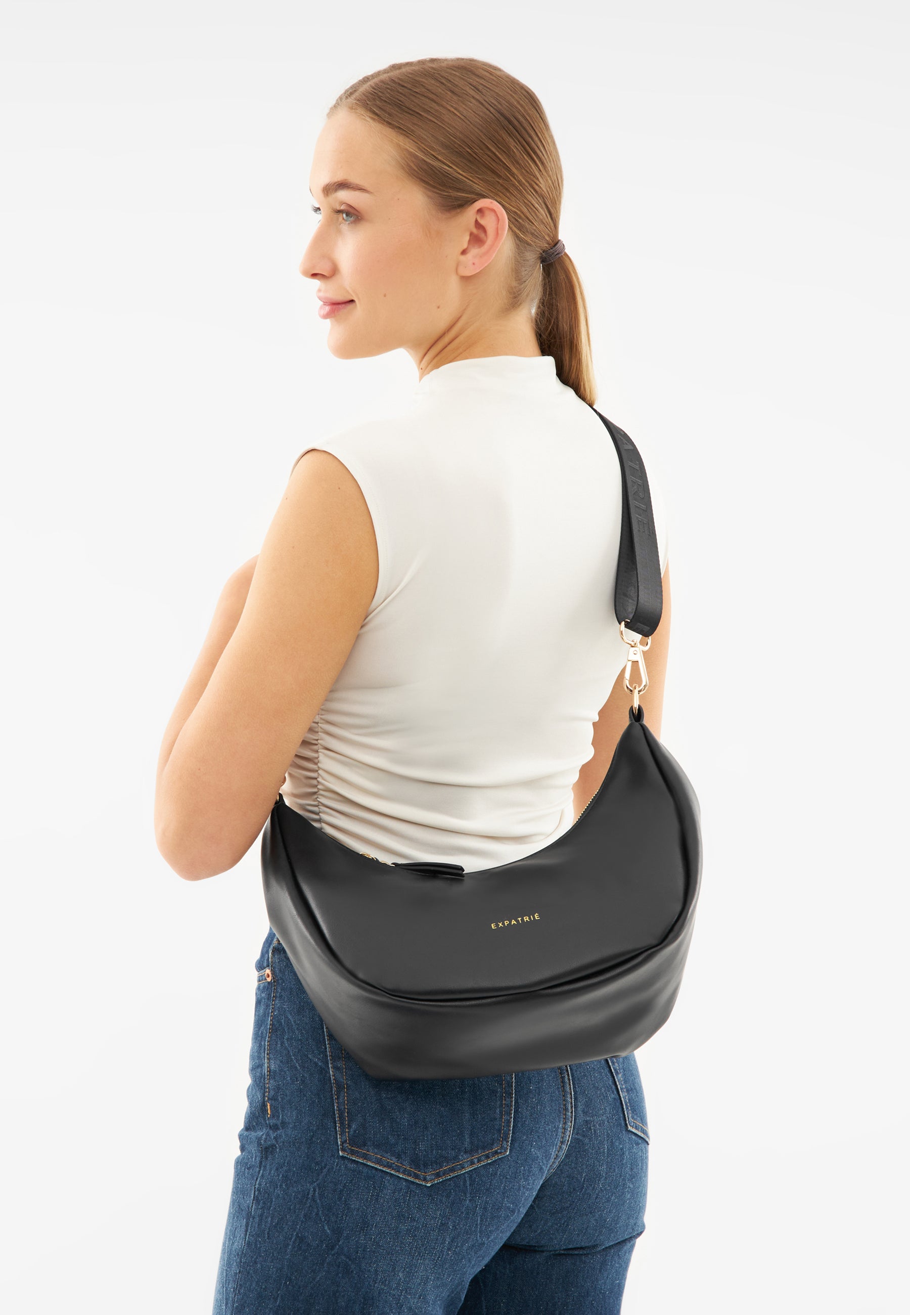 Frau mit weißem ärmellosem Oberteil und blauer Jeans trägt schwarze LEA MEDIUM Half Moon Tasche über der Schulter