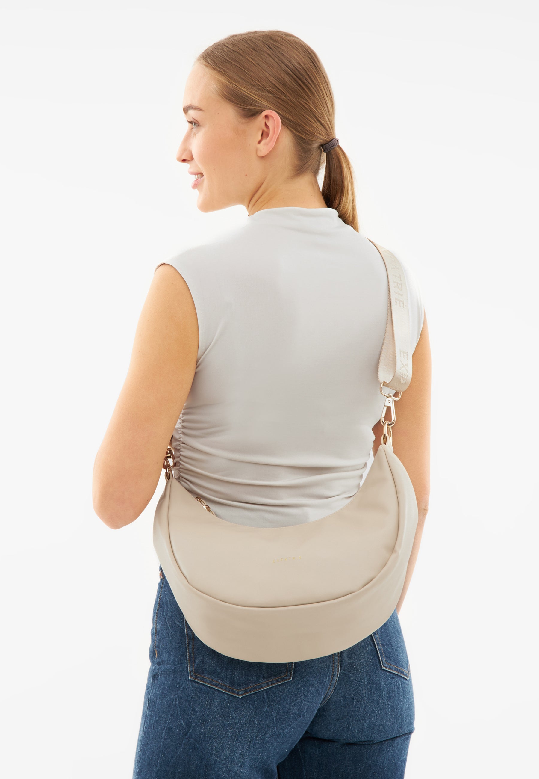 Frau von hinten mit halbmondförmiger, beigefarbener LEA MEDIUM - HALF MOON BAG Schultertasche und grauem ärmellosen Oberteil