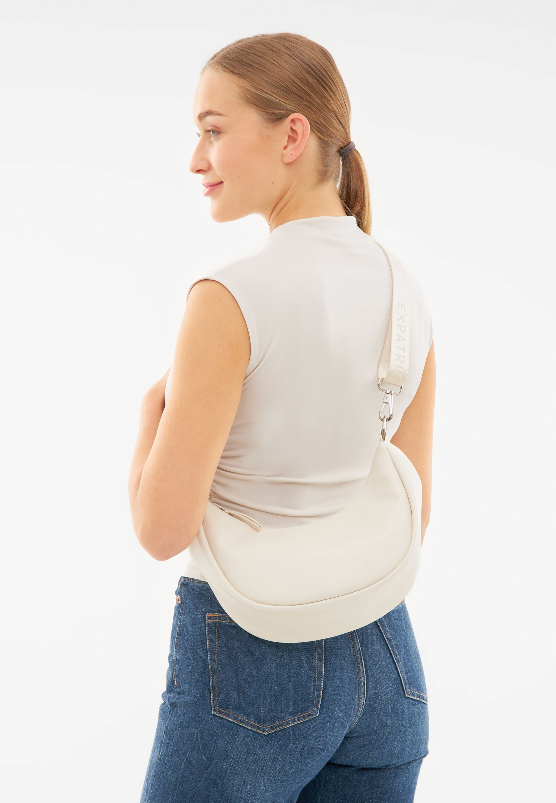 Frau mit cremefarbener LEA SMALL Half Moon Tasche über der Schulter, trägt ärmelloses Oberteil und Jeans