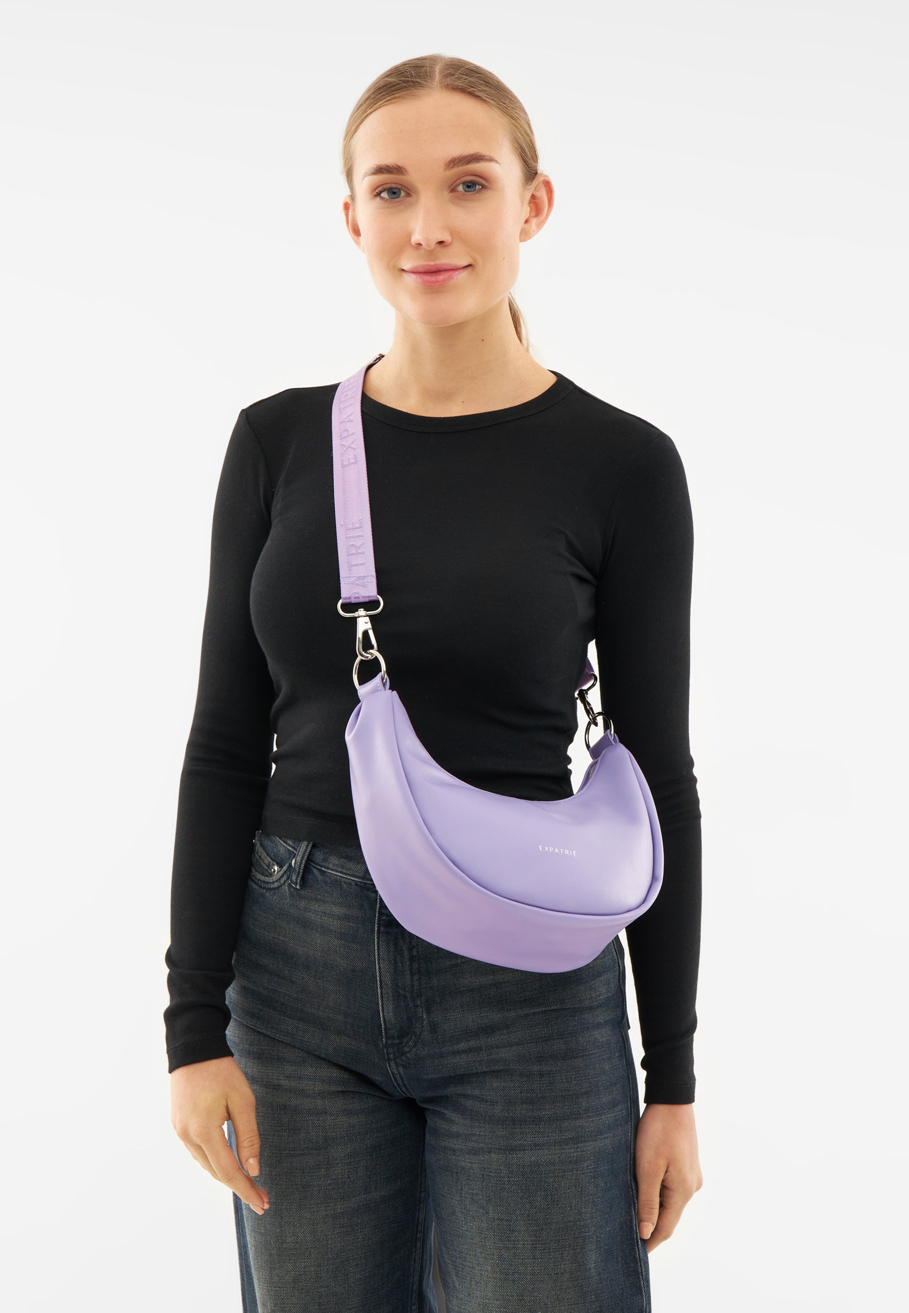 Frau mit schwarzem Oberteil und Jeans trägt lilafarbene LEA SMALL Halbmond-Tasche von Expatrié über der Schulter