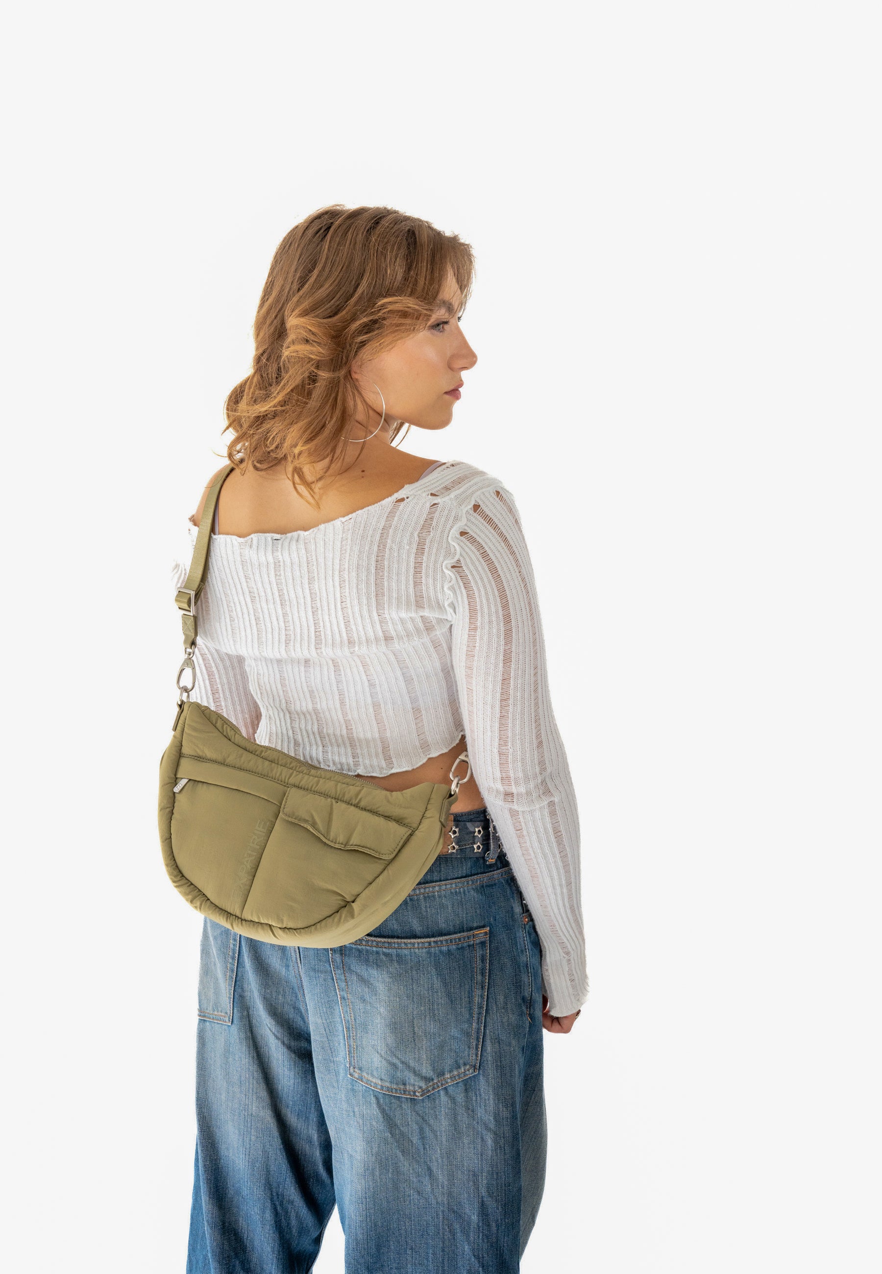 Frau trägt olivgrüne VIVY Half Moon Bag über der Schulter, weiße durchsichtige Bluse, blaue Jeans