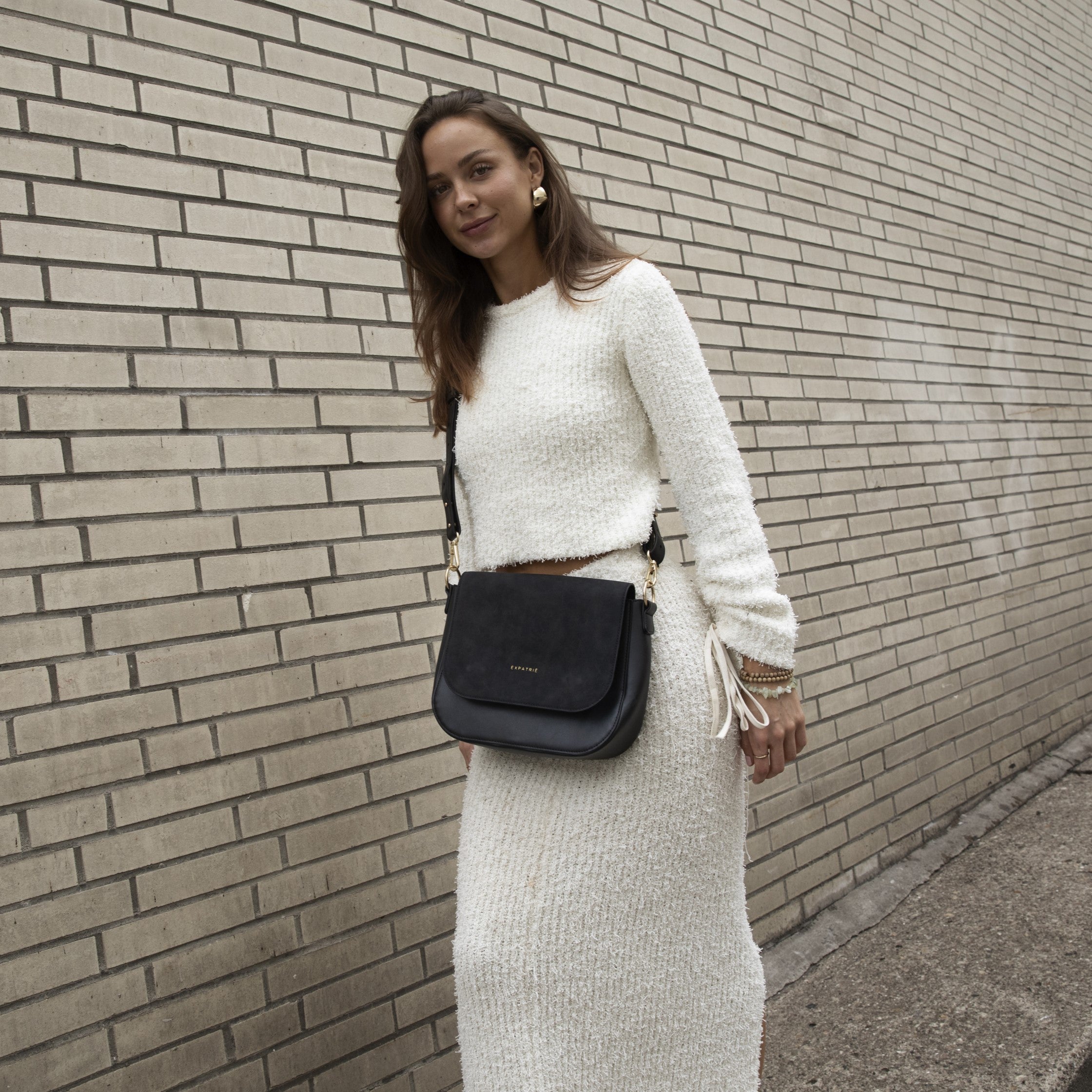 Frau trägt große schwarze Saddle Bag Louise aus Leder, Outfit in Cremefarben