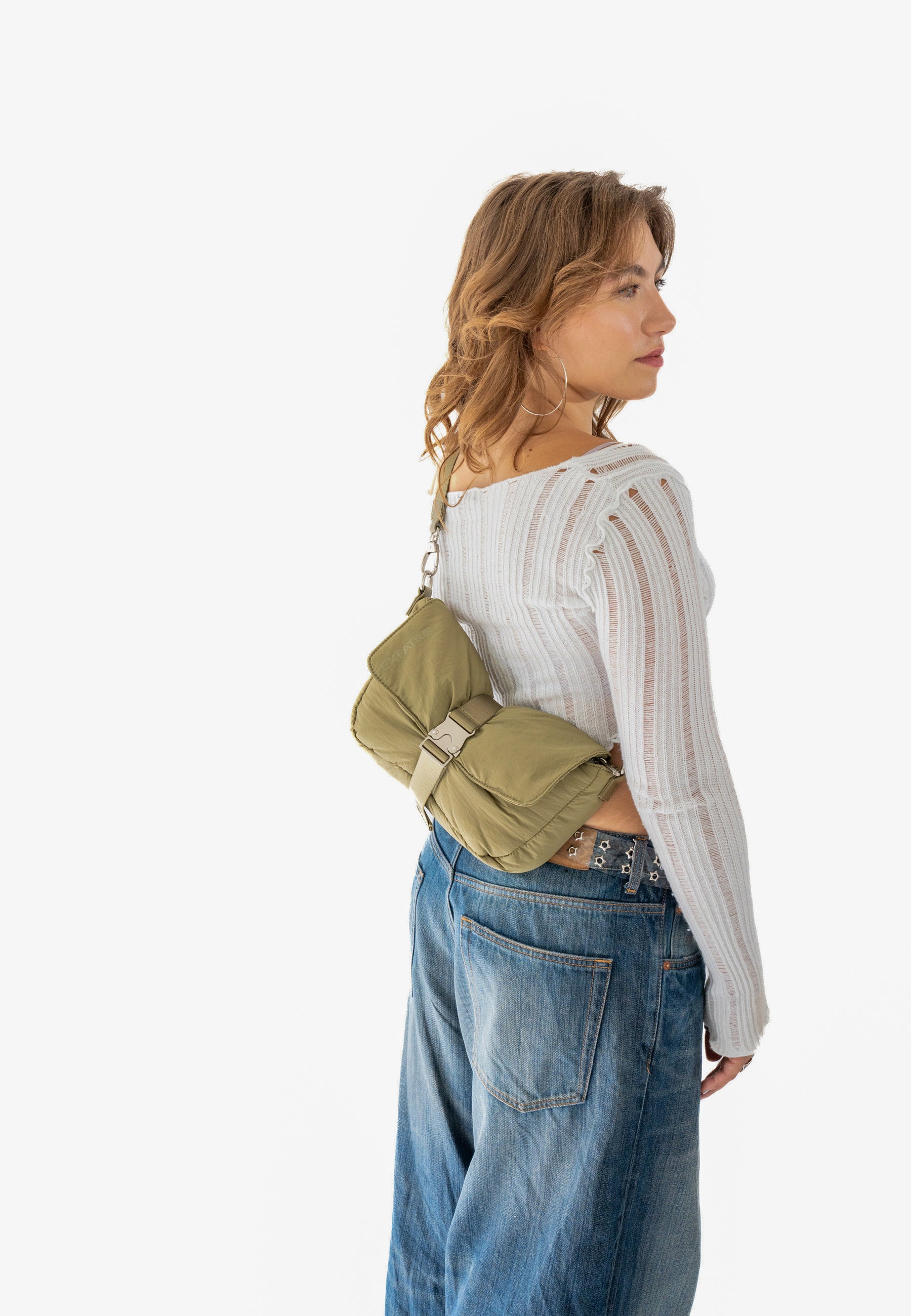 Frau trägt olivefarbene BOBBY Handtasche quer am Rücken mit weißem langärmligem Oberteil und blauen Jeans