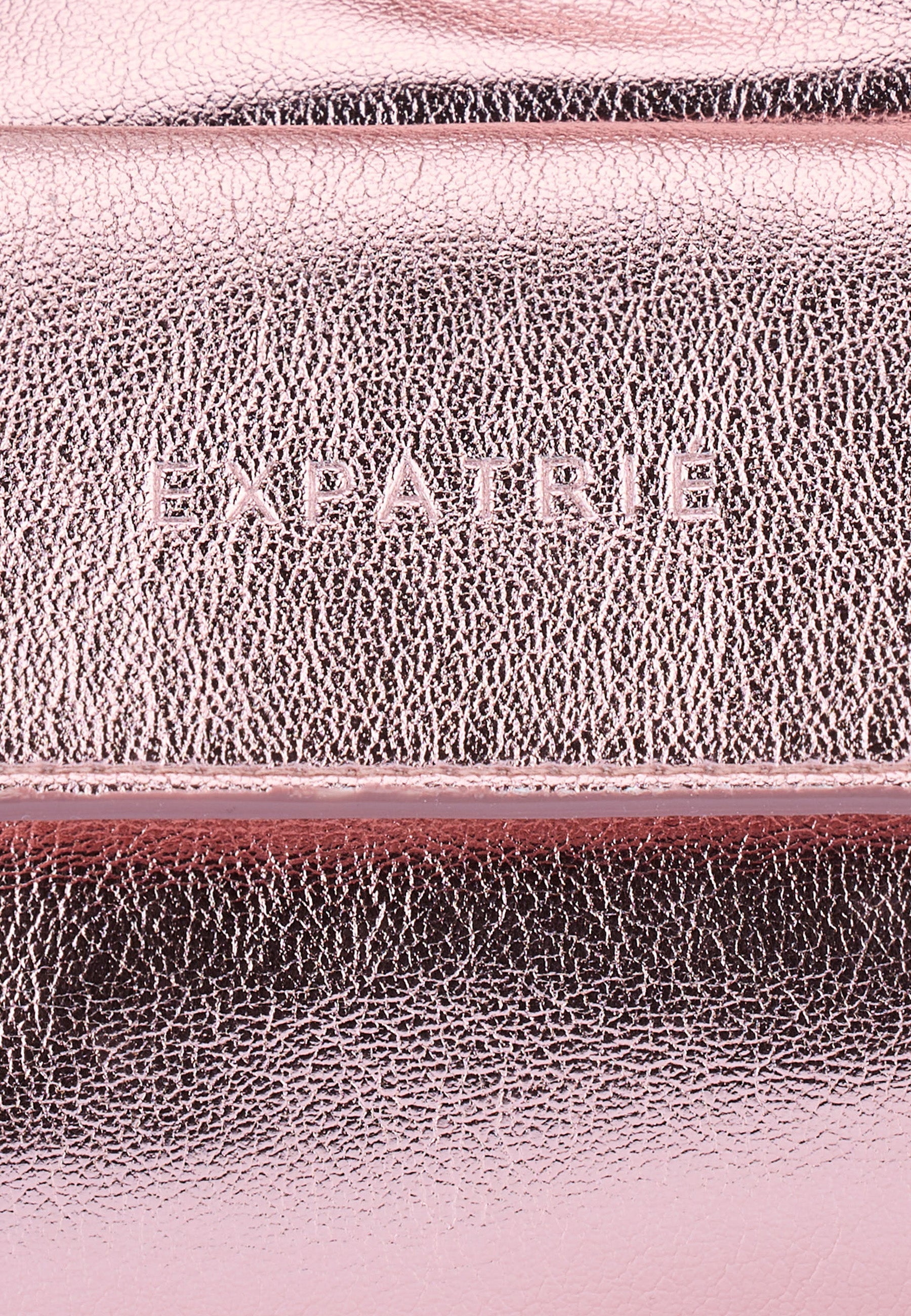 Nahaufnahme der rose-gold metallic Oberfläche der ELECTRA Handtasche mit eingeprägtem 'EXPATRIE' Logo