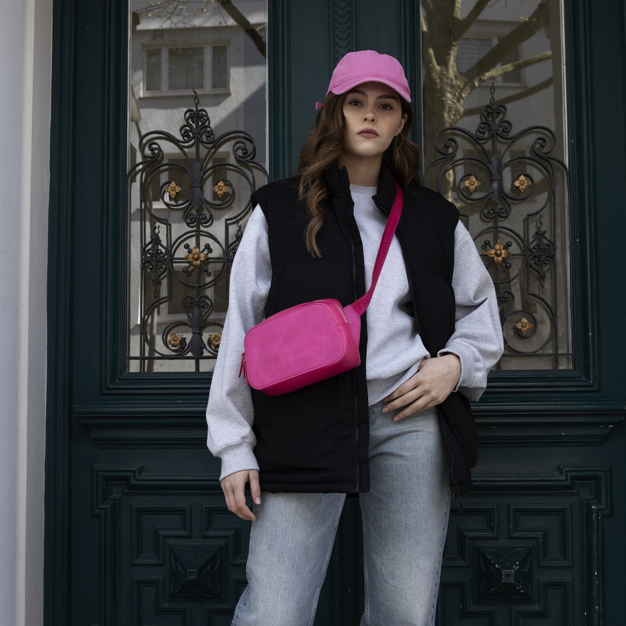 Frau trägt Umhängetasche Fleur pink aus Leder, kombiniert mit schwarzer Weste und grauem Pullover