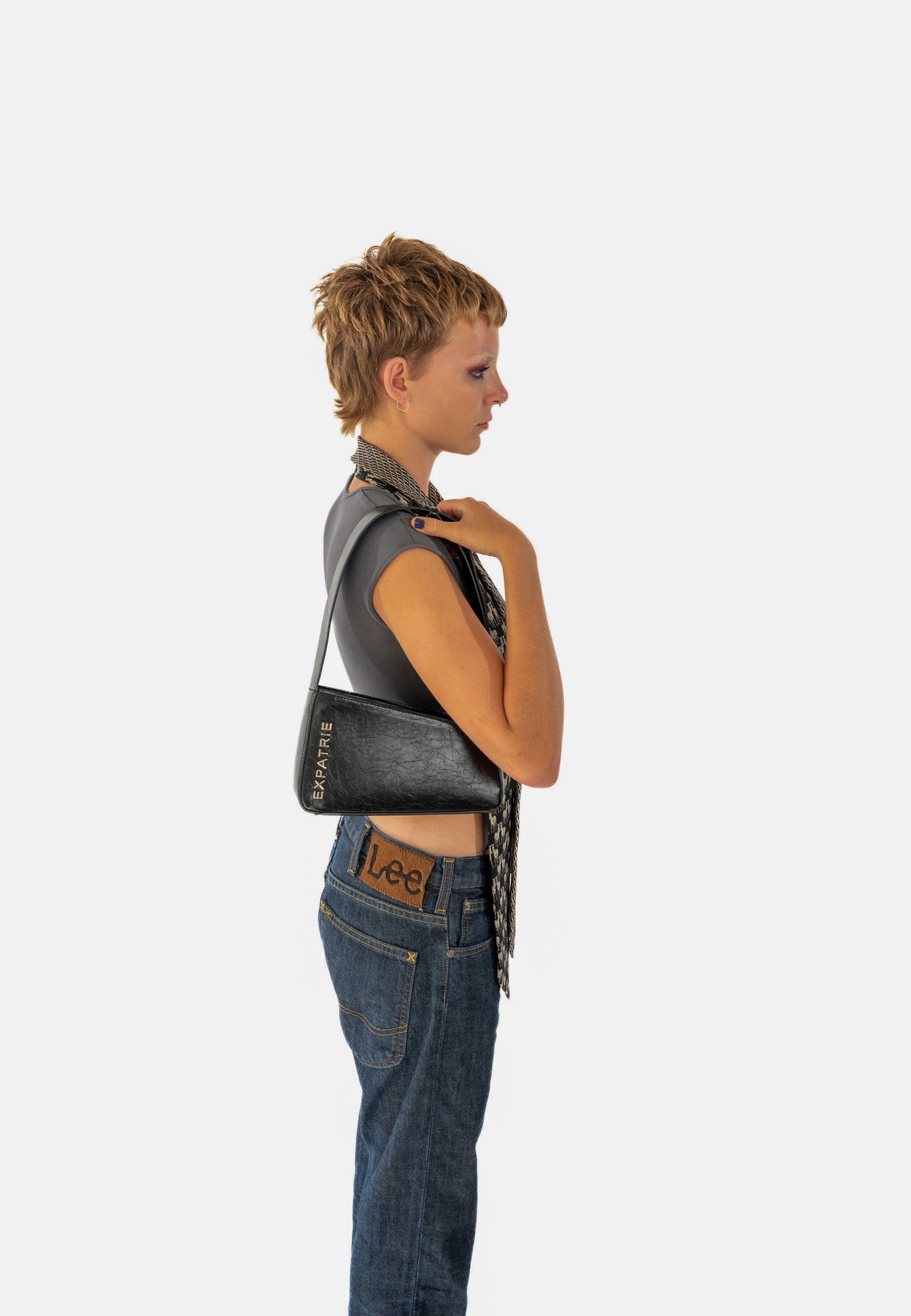 Frau trägt schwarze Georgia Handtasche von Expatrié über der Schulter, vintage Look, kombiniert mit dunklen Jeans und kurzem Top