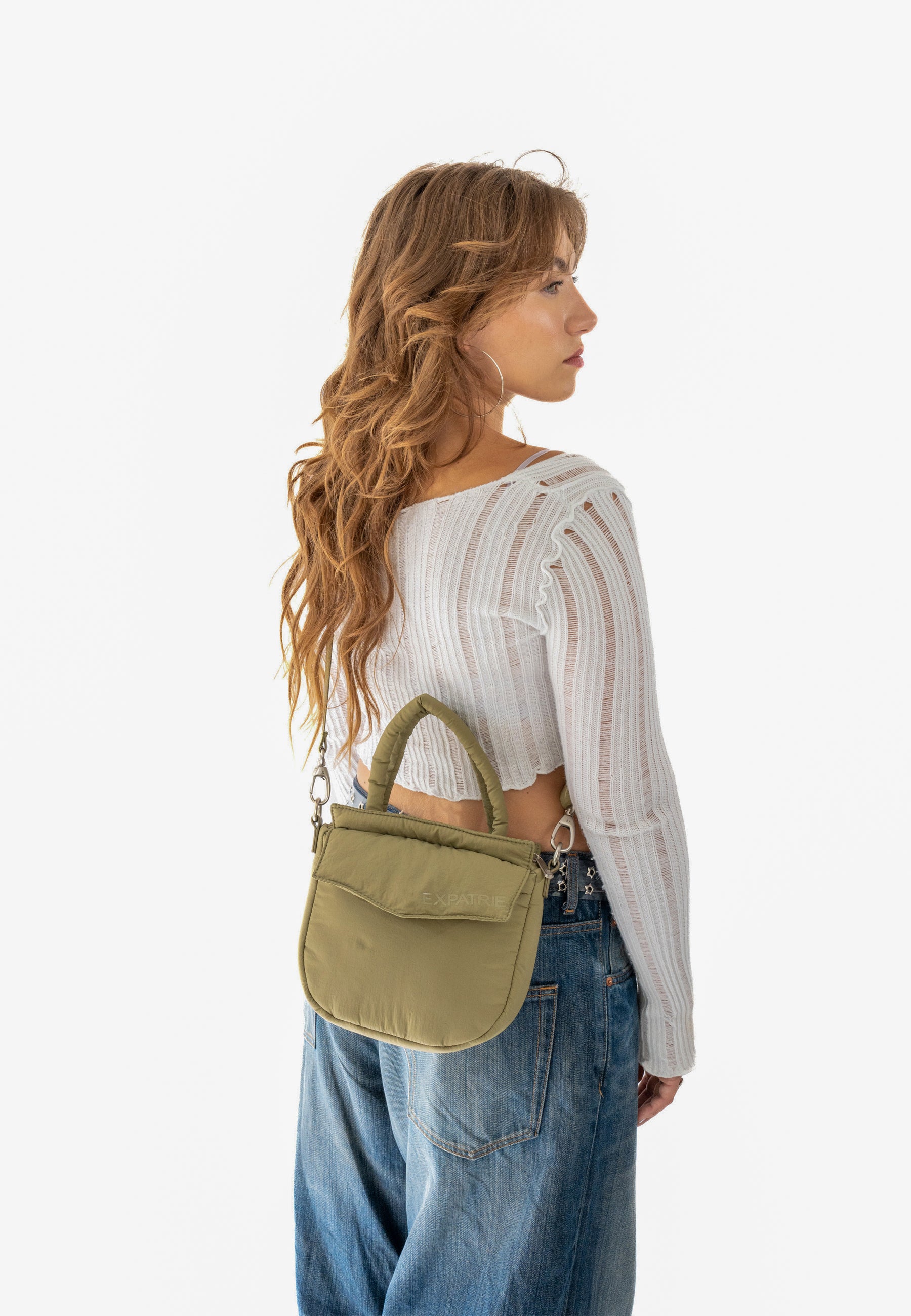 Frau mit langem, lockigem Haar trägt olivefarbene Poppy Small Handtasche und weiße, leichte Strickjacke