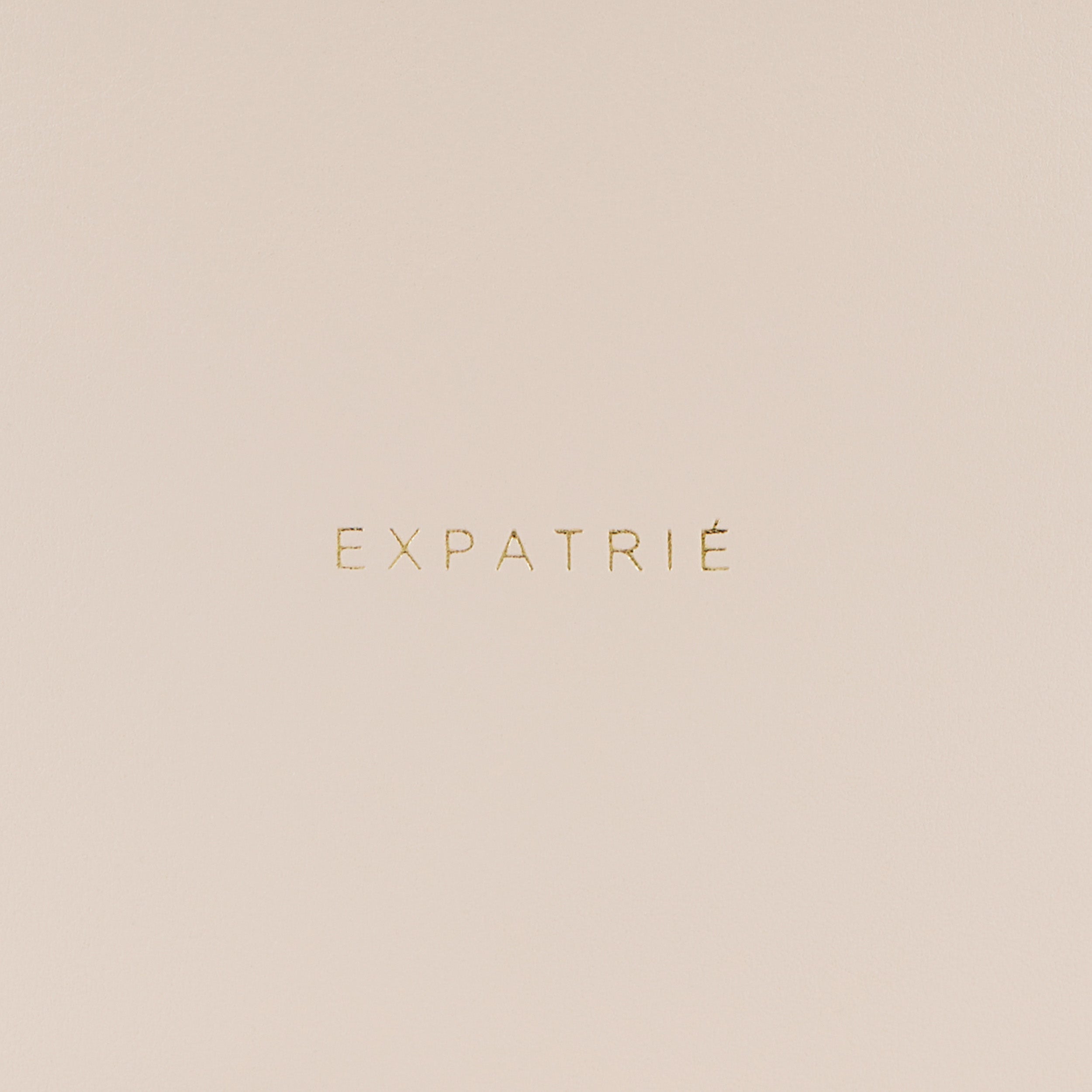 Brandlogo 'EXPATRIÉ' in gold auf beigem Hintergrund