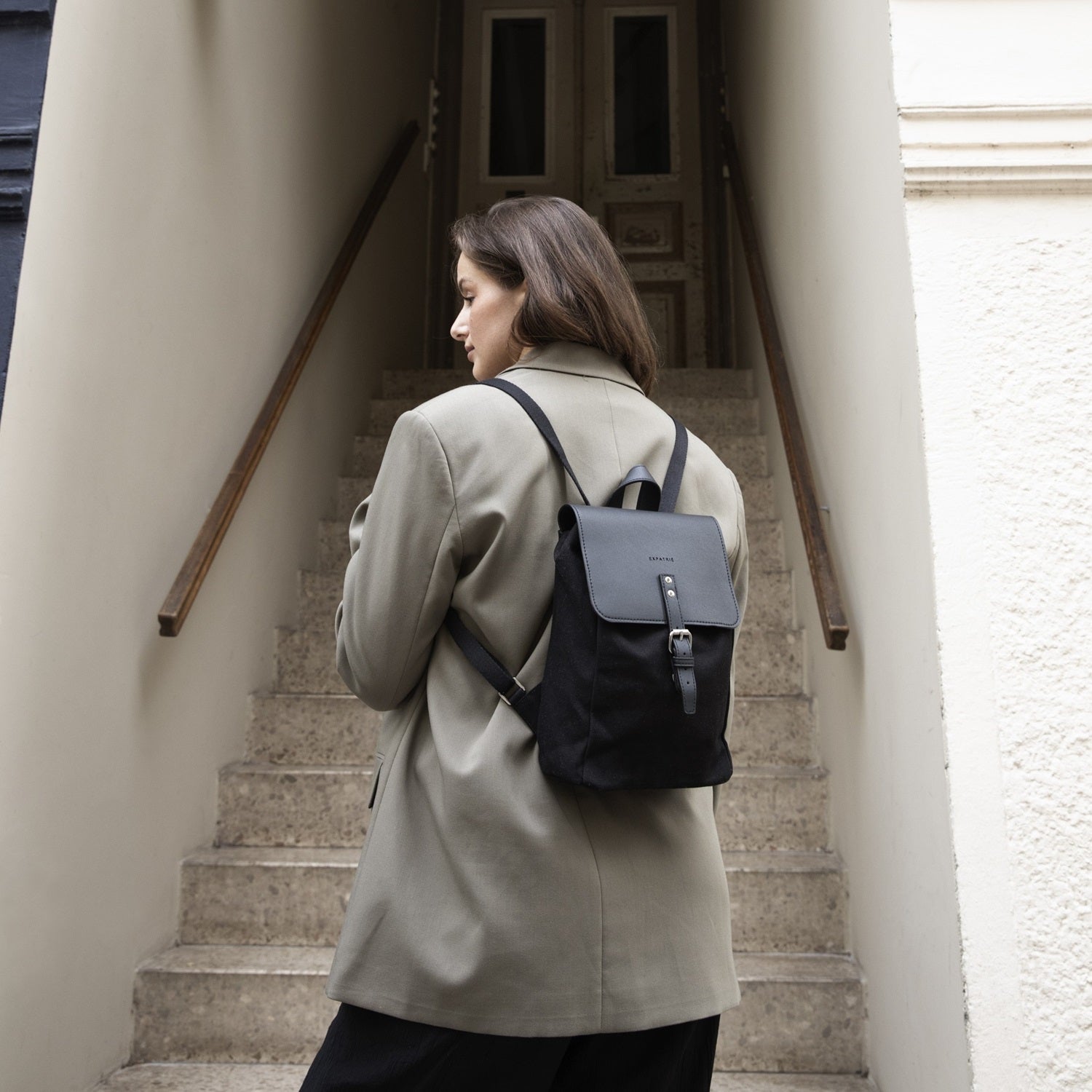 Frau mit grünem Blazer trägt den schwarzen Mini Rucksack 'Anna' mit Lederverschluss auf dem Rücken