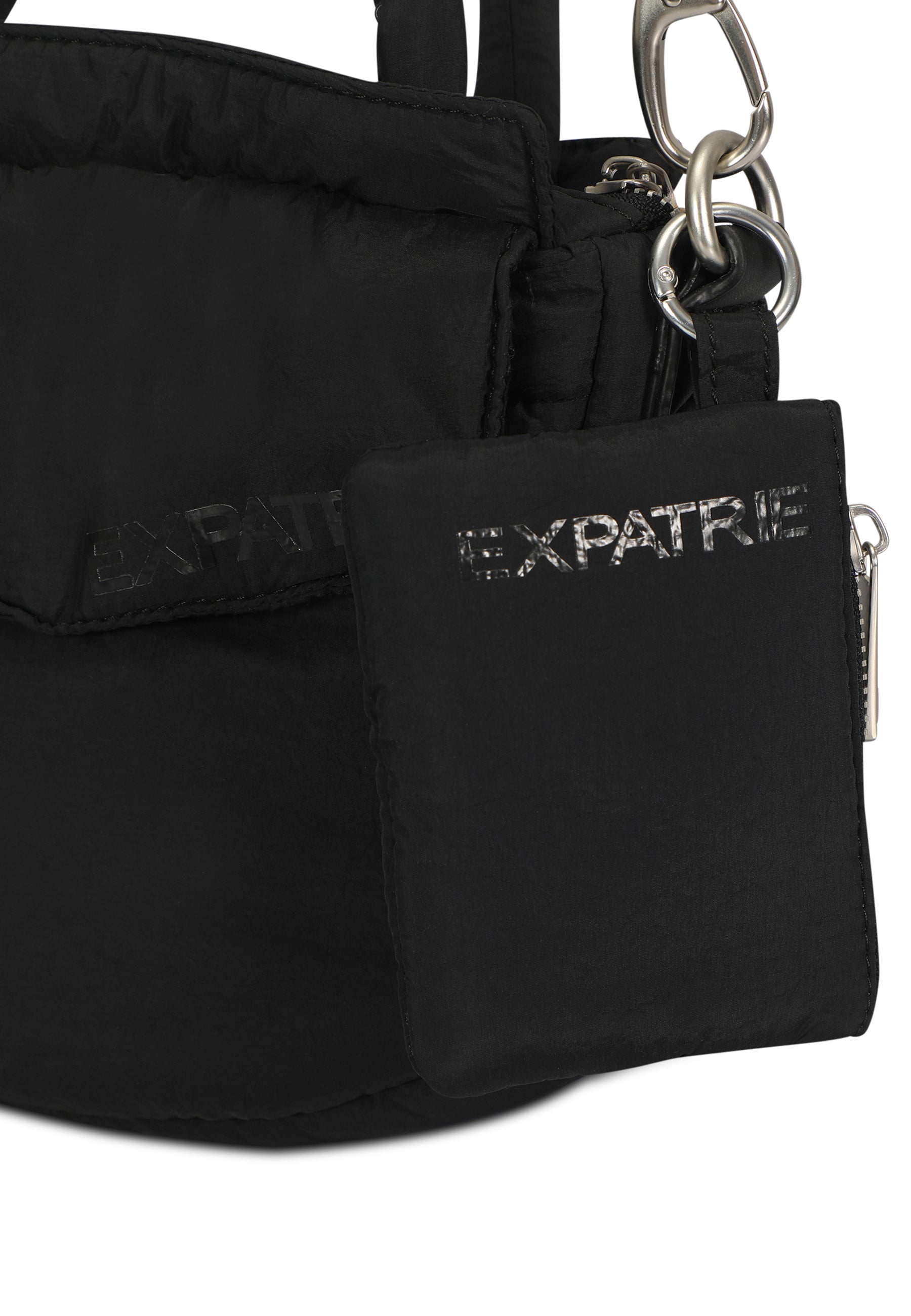 Schwarzes Mini Portemonnaie mit silbernem 'EXPATRIE' Logo und Reißverschluss, befestigt an einem schwarzen Rucksack