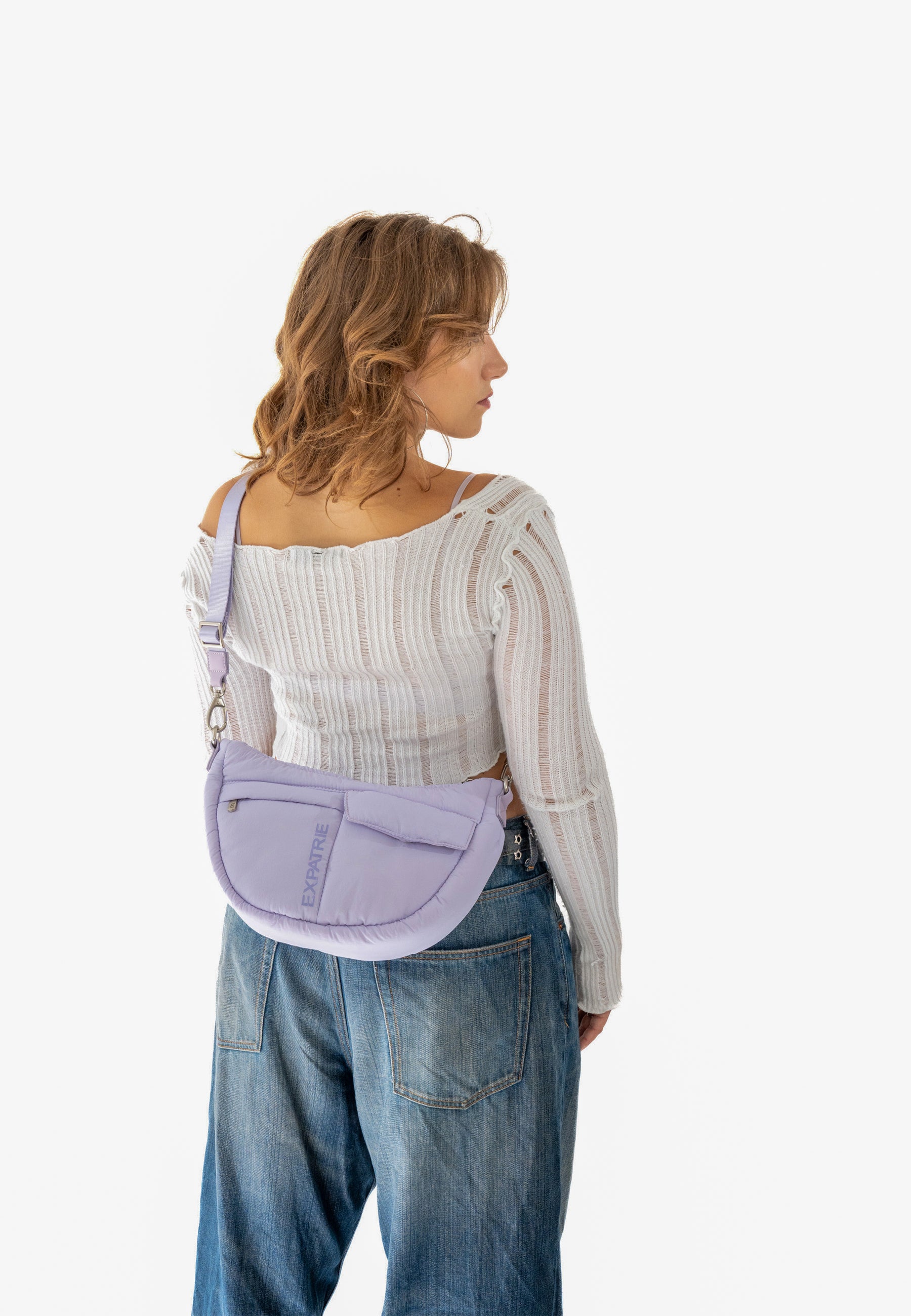 Frau mit lockerem, weißem Rippenpullover und blauen Jeans trägt lilafarbene VIVY Half Moon Tasche über der Schulter