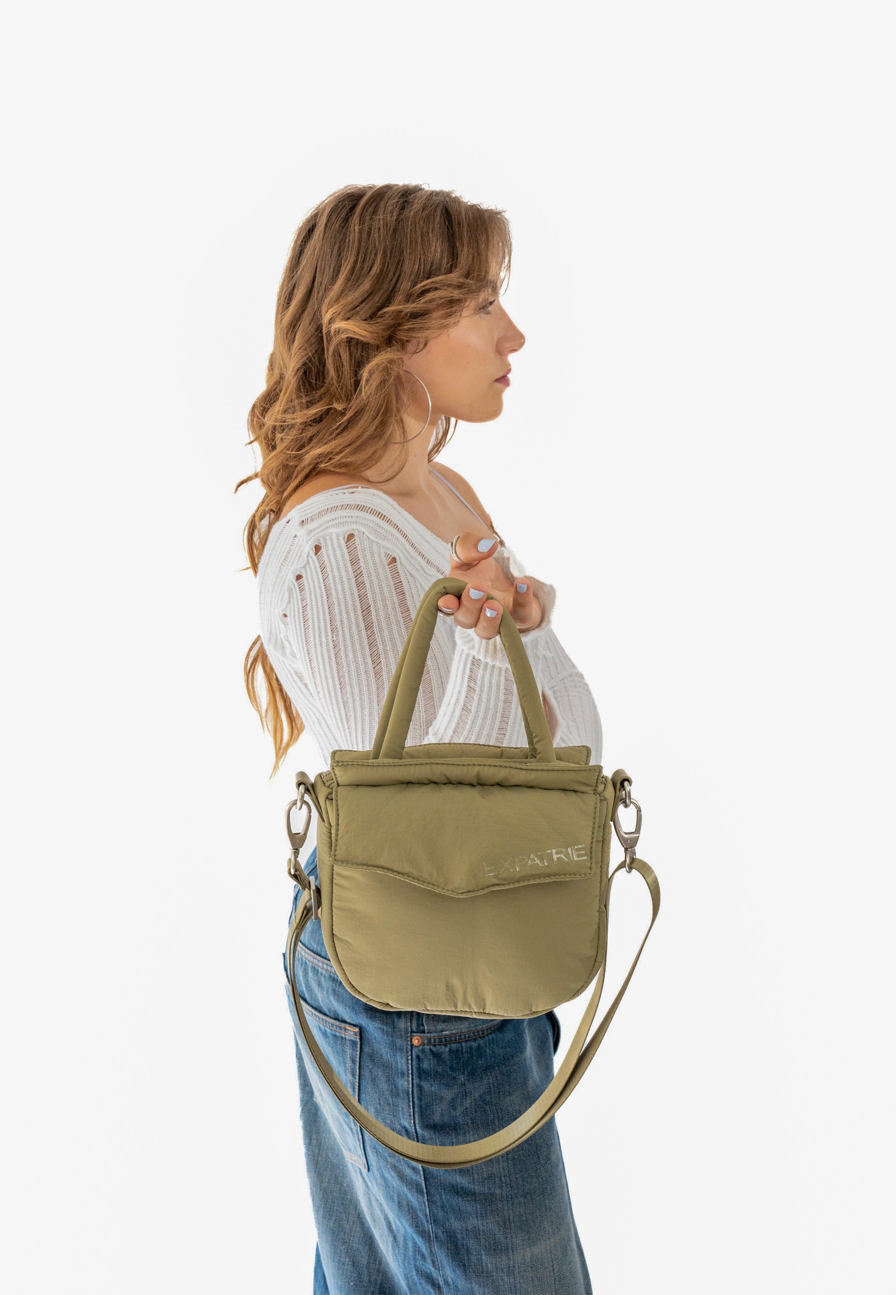 Frau in weißem Pullover hält olivgrüne POPPY SMALL Handtasche von Expatrié in der Hand