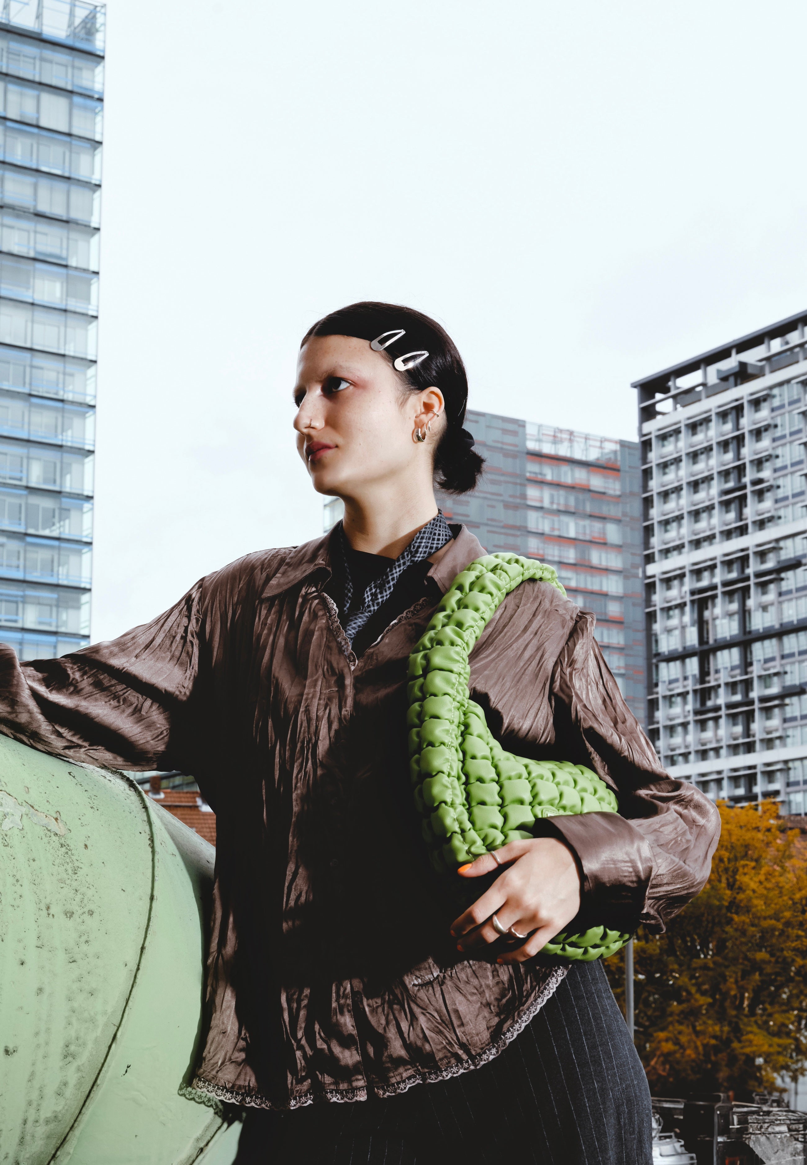 Frau mit brauner Bluse und grüner PIPPA LARGE Handtasche vor städtischer Skyline