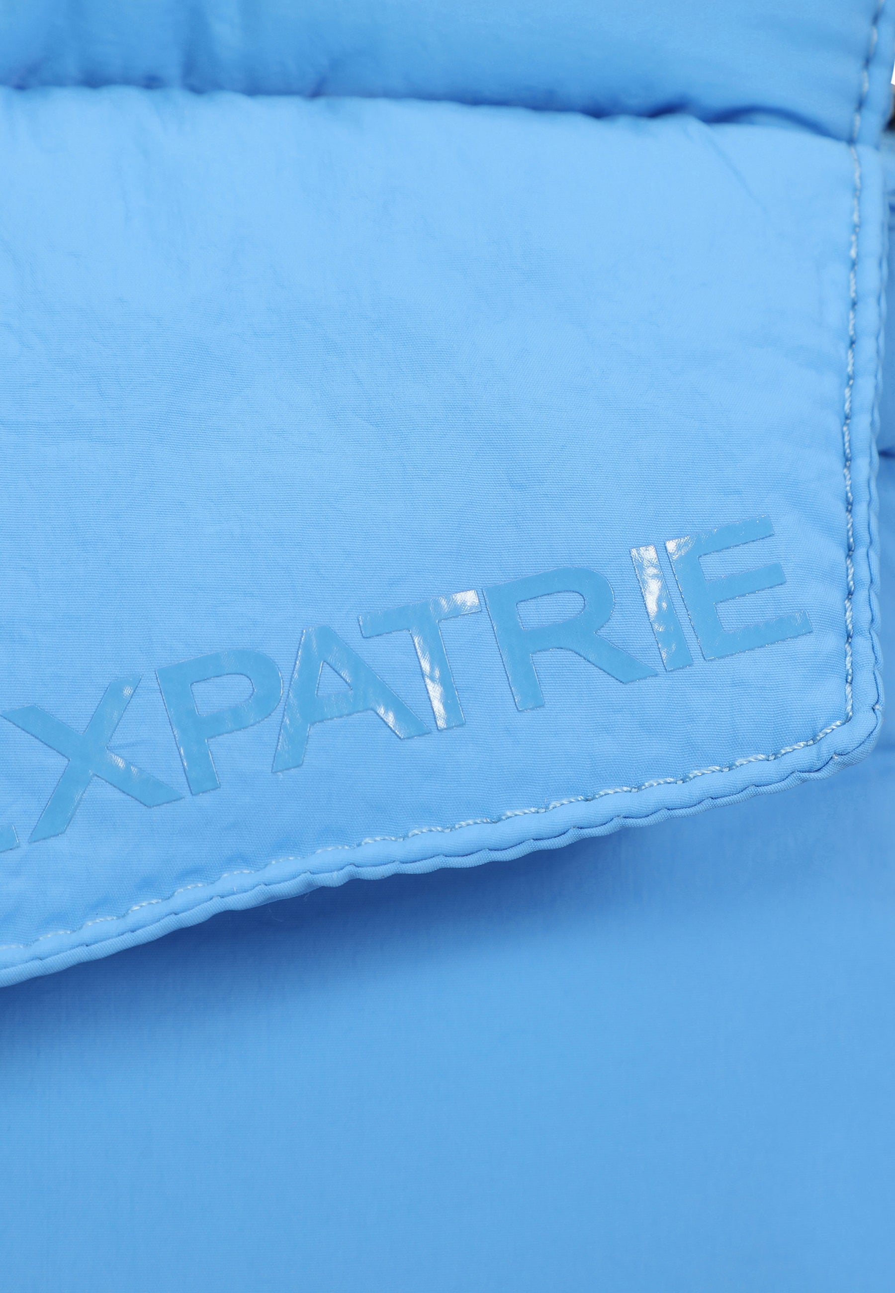 Nahaufnahme der blauen POPPY SMALL Handtasche mit glänzendem 'EXPATRIE' Logo