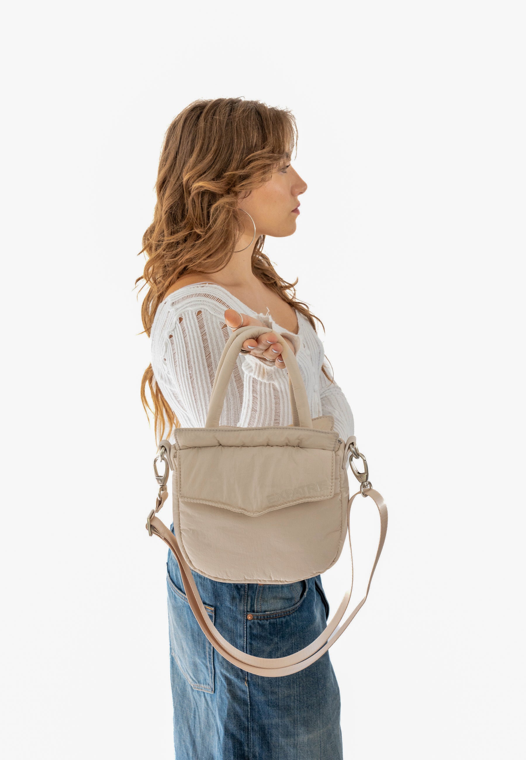 Frau hält beige Poppy Small Handtasche mit Griffen und verstellbarem Schulterriemen
