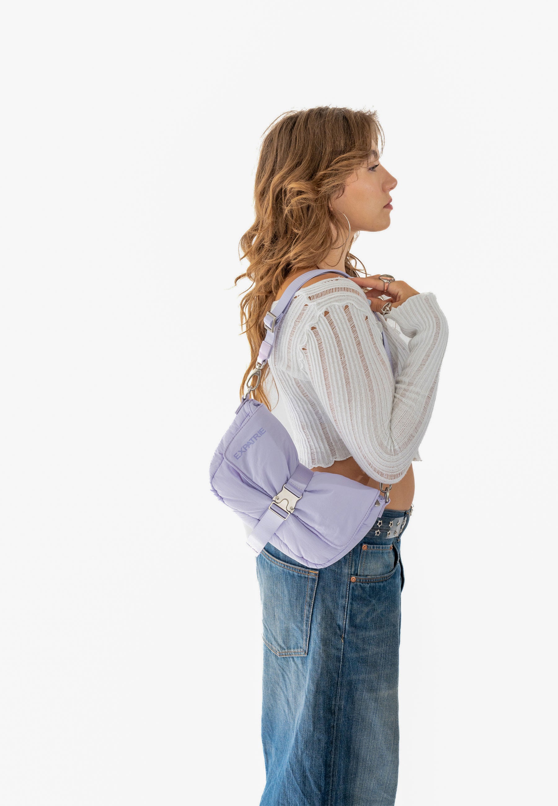 Seitliches Porträt einer Frau mit lockigem Haar, die einen lila BOBBY Handtasche aus Puffer-Material über der Schulter trägt