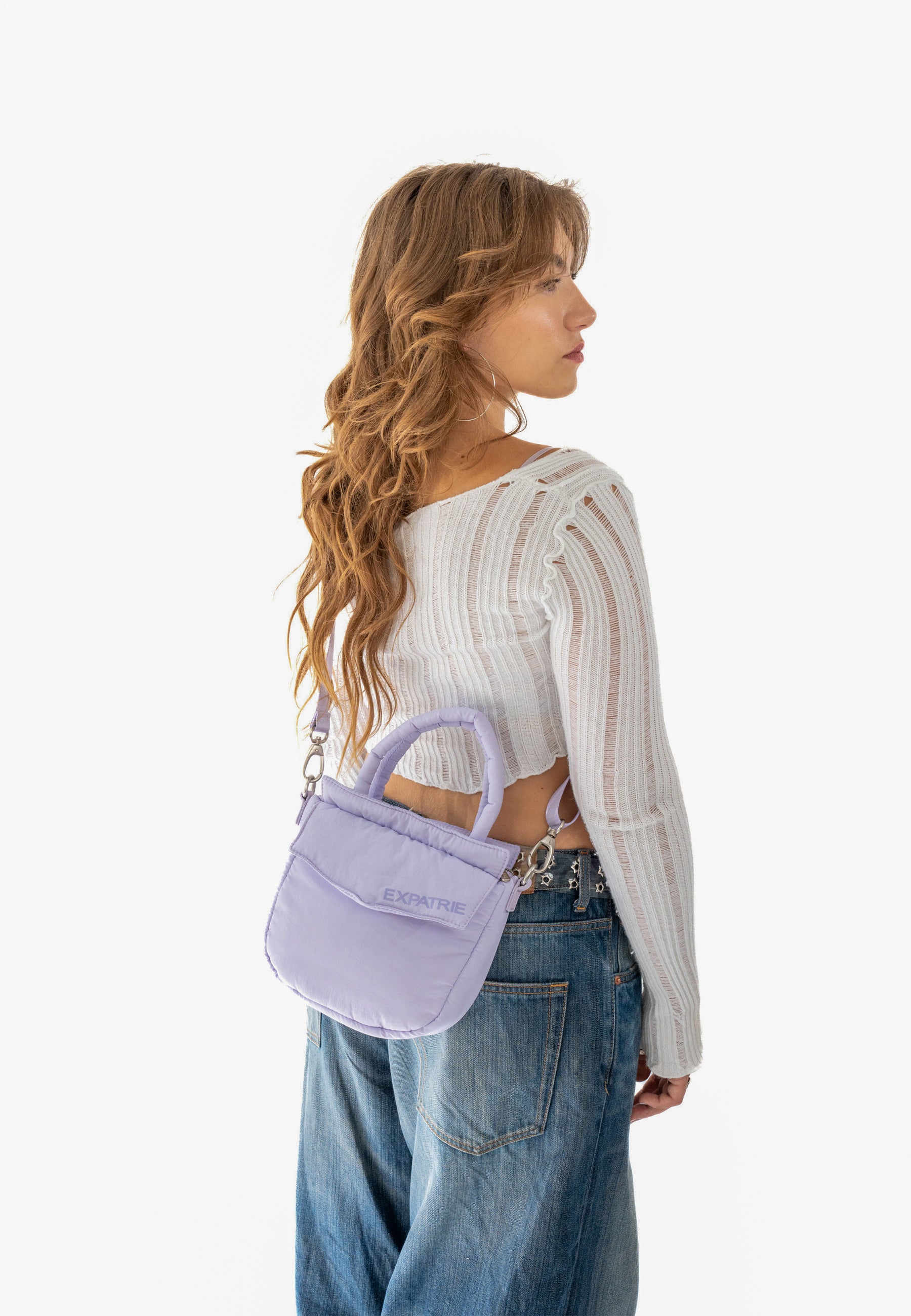 Damen trägt lilafarbene Puffer-Handtasche 'POPPY SMALL' von Expatrié mit kurzem Griff und verstellbarem Schulterriemen