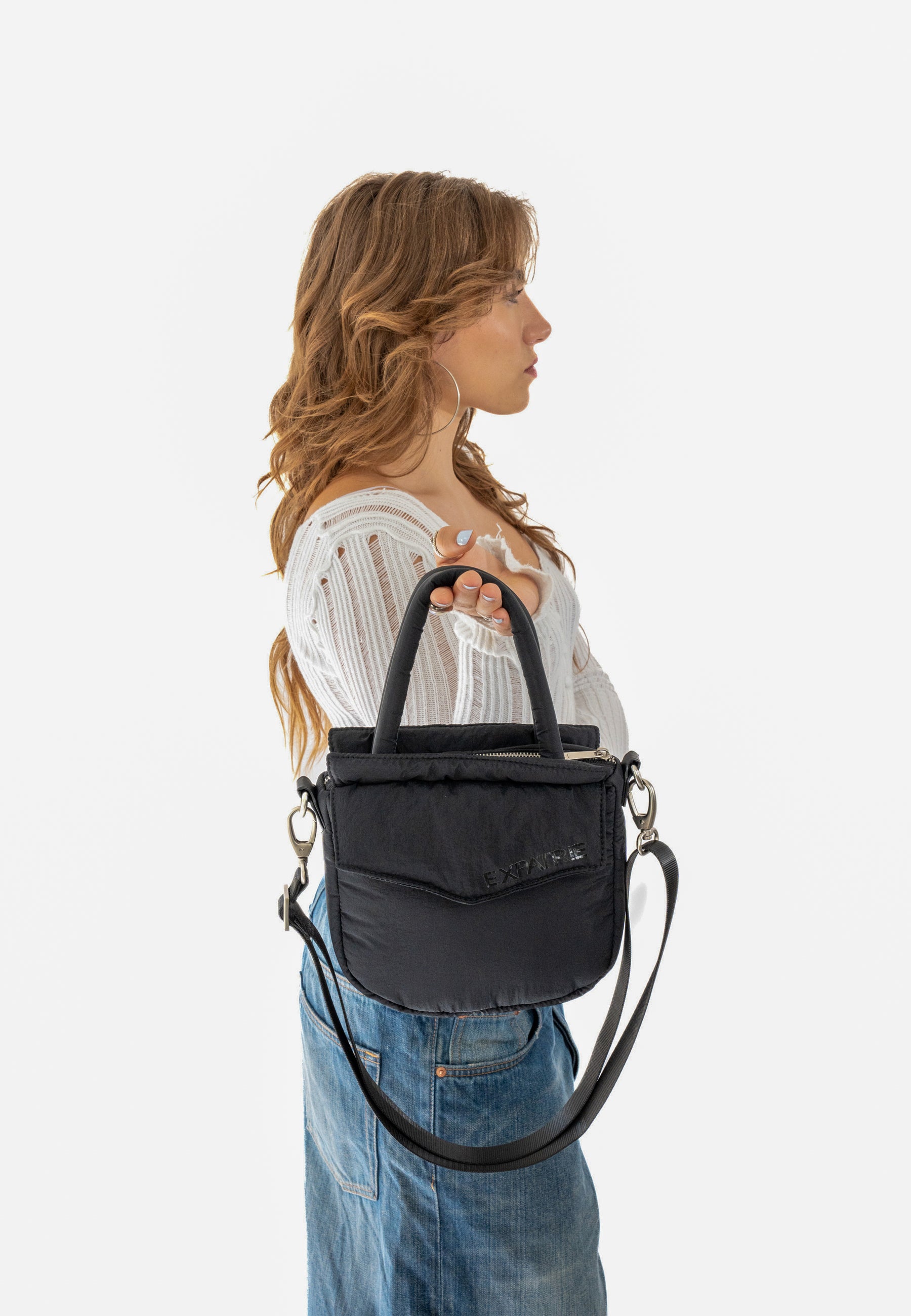 Frau hält schwarze gepolsterte Poppy Small Handtasche mit Griffen und abnehmbarem Schulterriemen