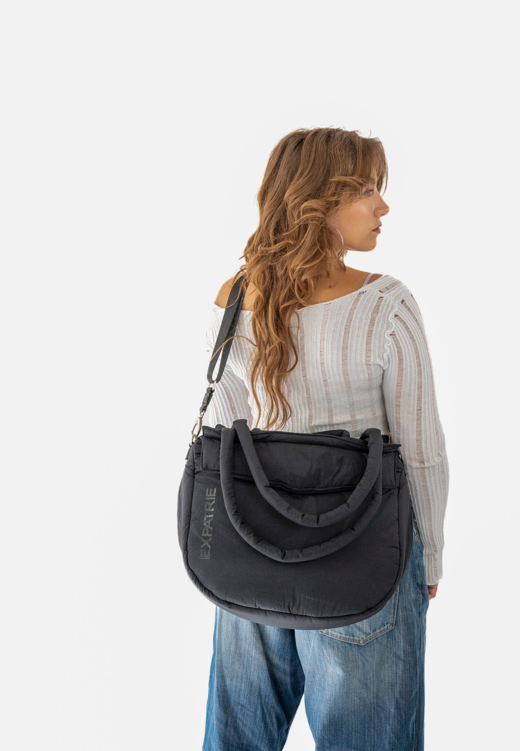 Frau mit lockigen Haaren trägt schwarze POPPY Shopper Tasche von Expatrié über der Schulter