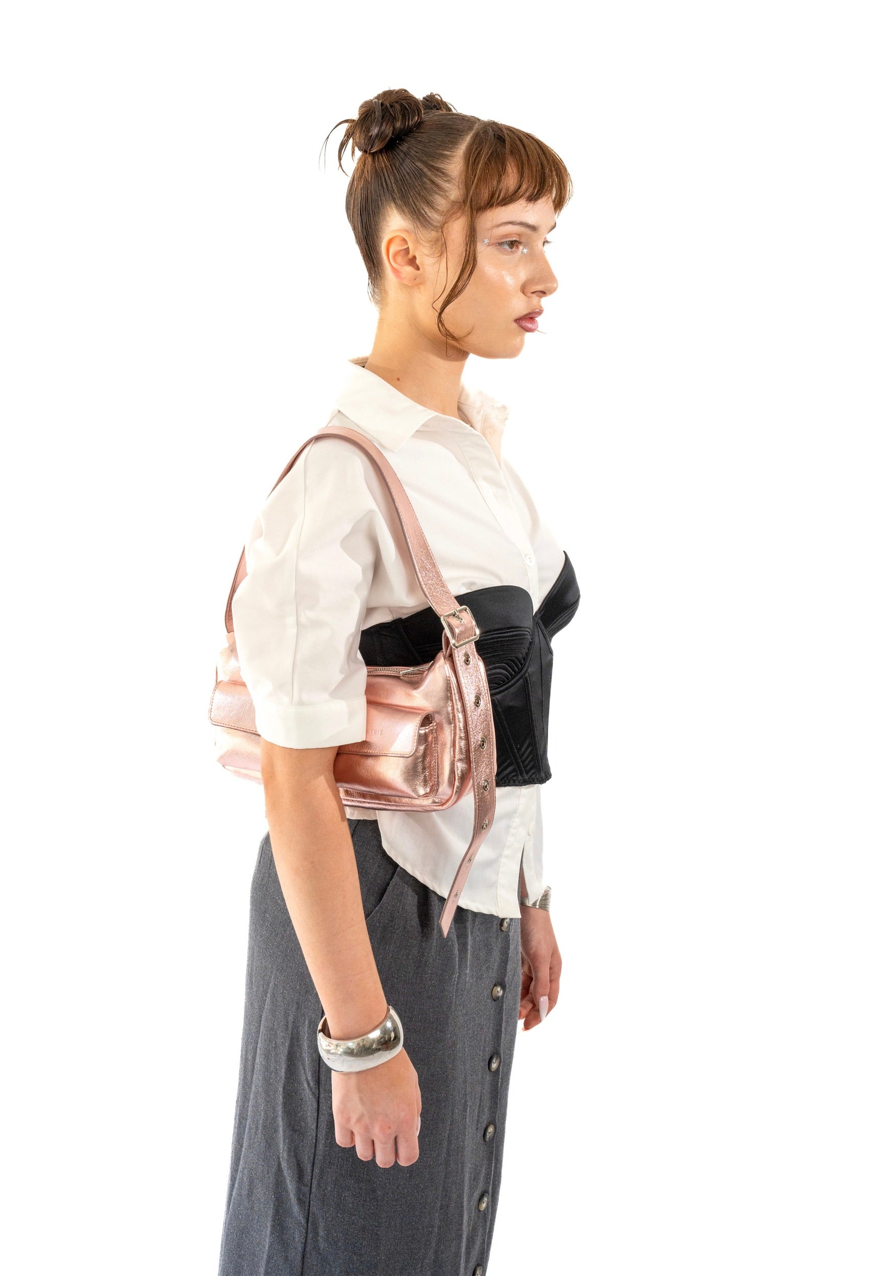 Seitenansicht einer Frau mit hochgestecktem Haar, die eine rosa-goldene Metallic-Handtasche der Marke ELECTRA über der Schulter trägt