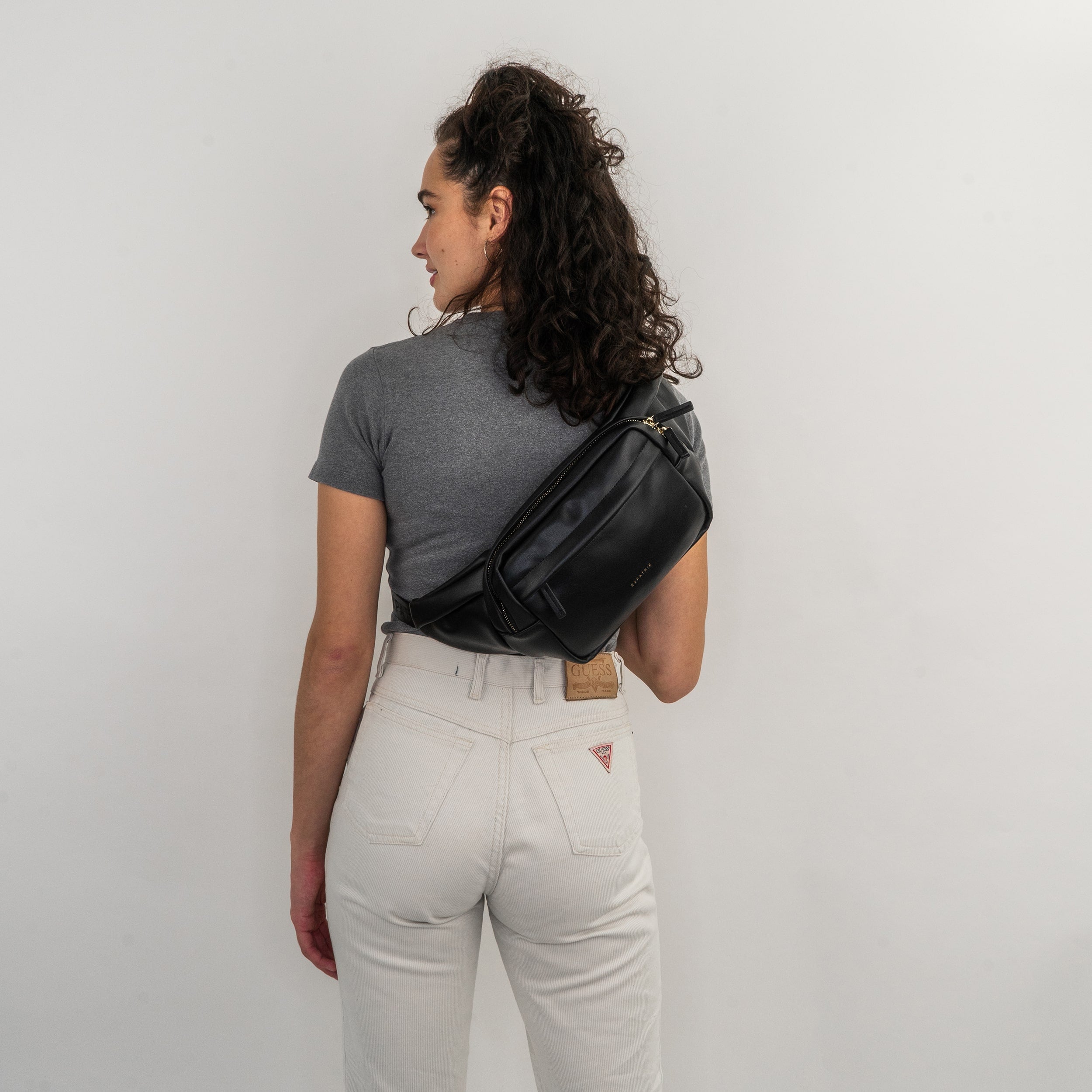 Frau von hinten mit grauem T-Shirt und heller Hose trägt schwarze Bauchtasche Justine PU quer über den Rücken