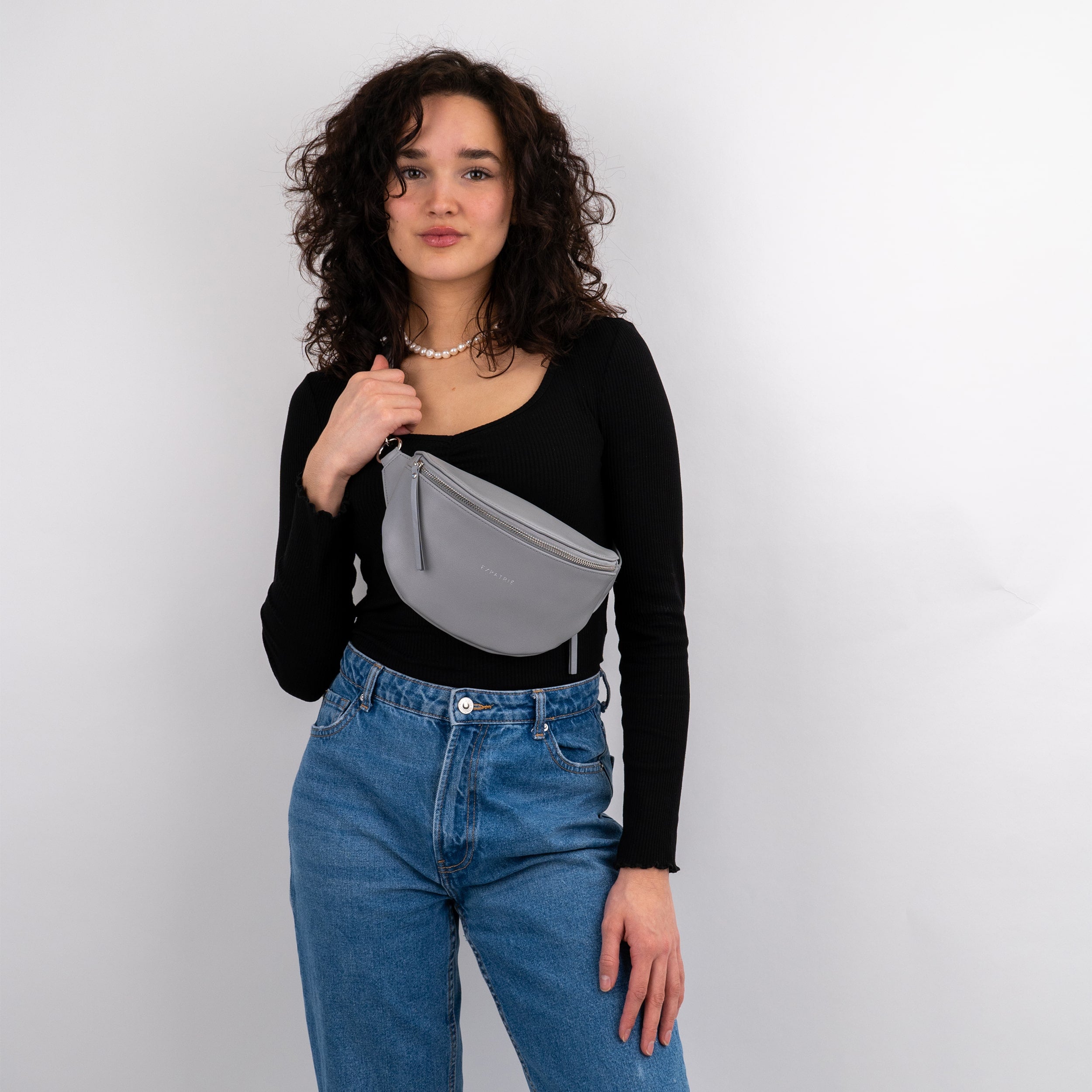 Frau trägt graue Bauchtasche Alice Small aus Leder über schwarzem Oberteil und blauer Jeans