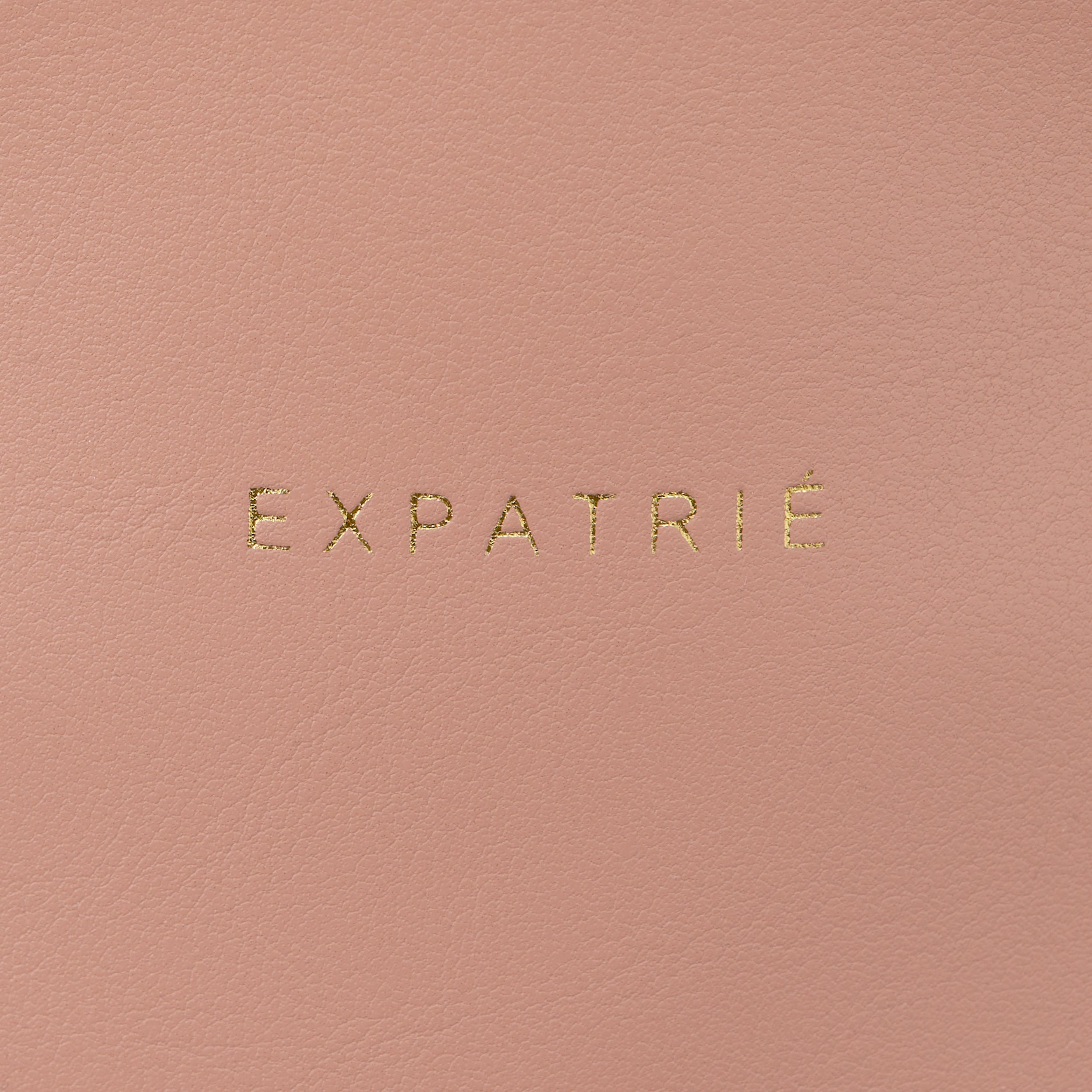 Nahaufnahme des goldenen EXPATRIÉ-Logos auf rosa Kunstleder der Bauchtasche Alice Small