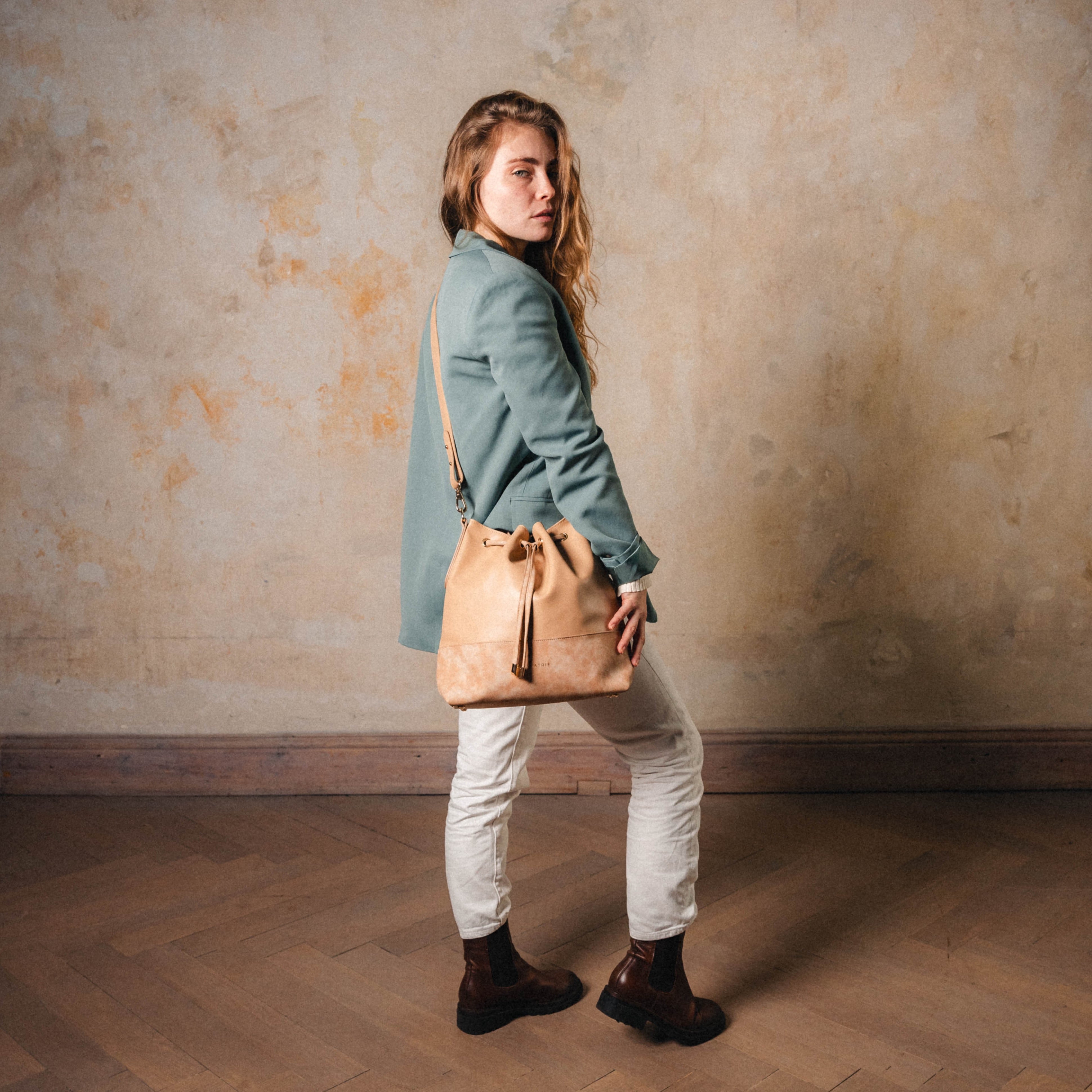 Beuteltasche Sarah in Beige aus Leder mit Kordelzug, getragen von Frau in grünem Blazer und weißen Hosen