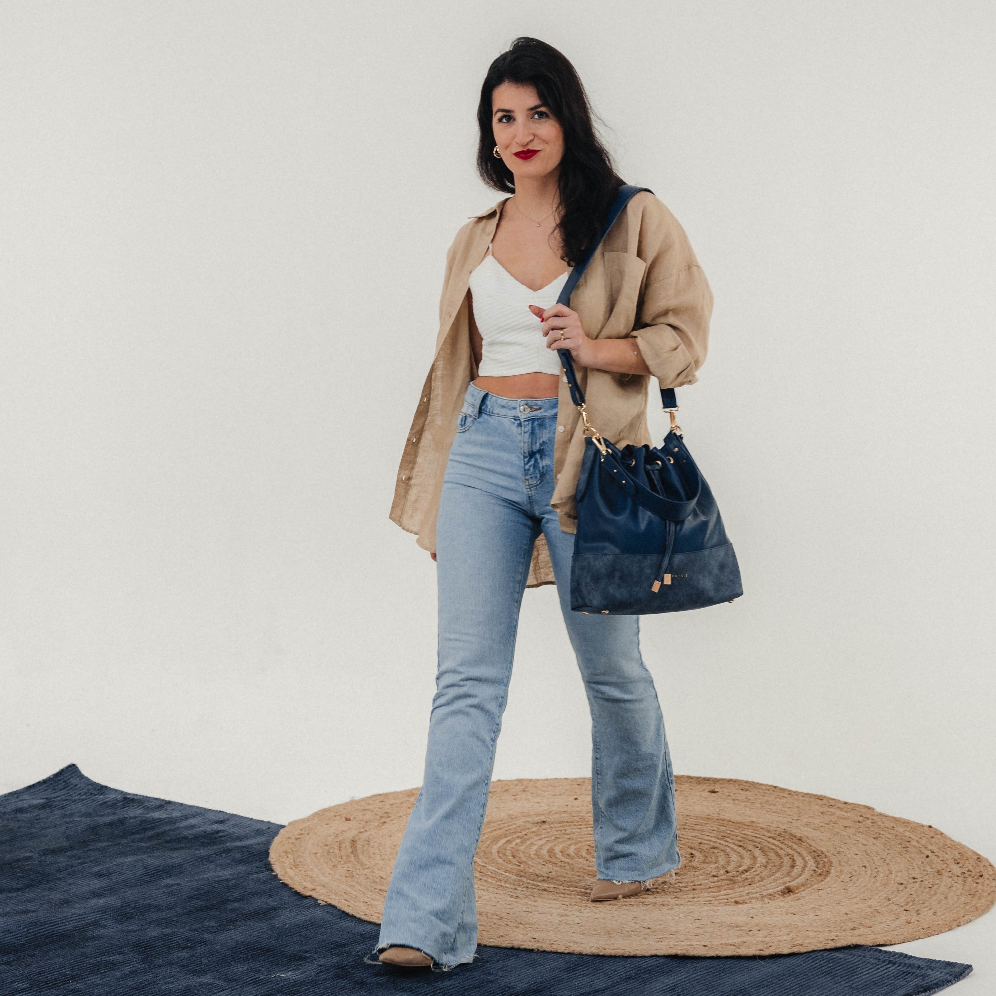 Frau mit Beuteltasche Sarah in dunkelblauem Leder, kombiniert zu beige Hemd und blauem Jeans