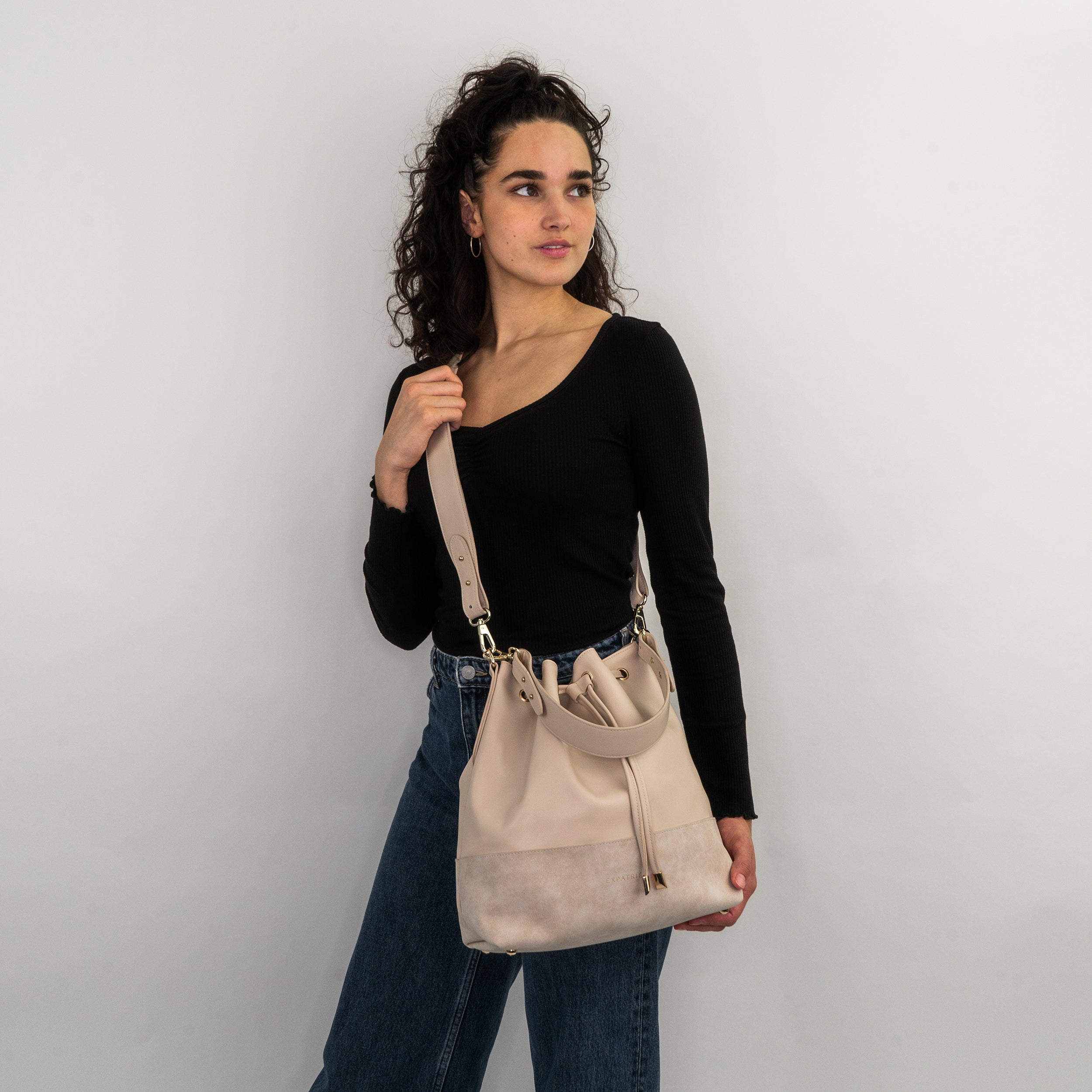 Frau mit schwarzen Oberteil und Jeans trägt beige Beuteltasche Sarah von Expatrié an der Schulter