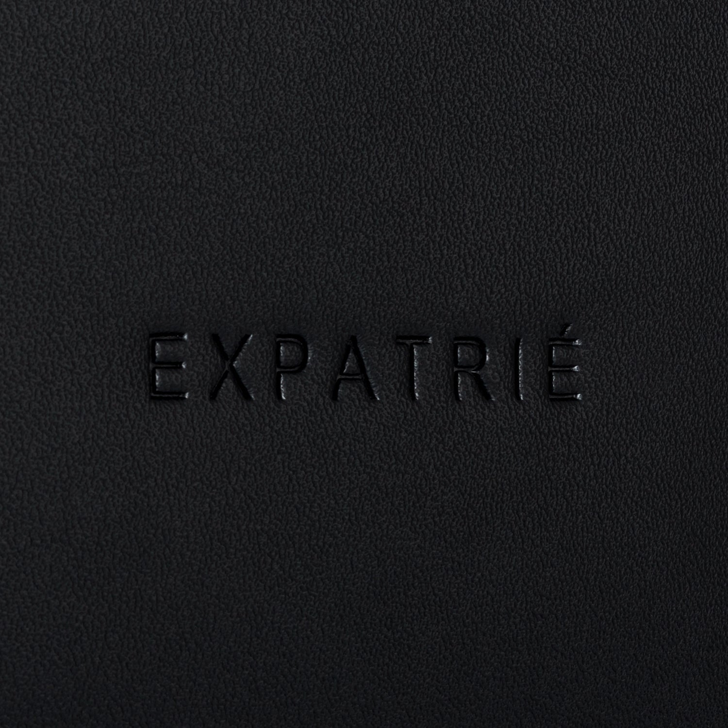 Schwarzes Kunstleder mit eingeprägtem Schriftzug 'EXPATRIÉ'
